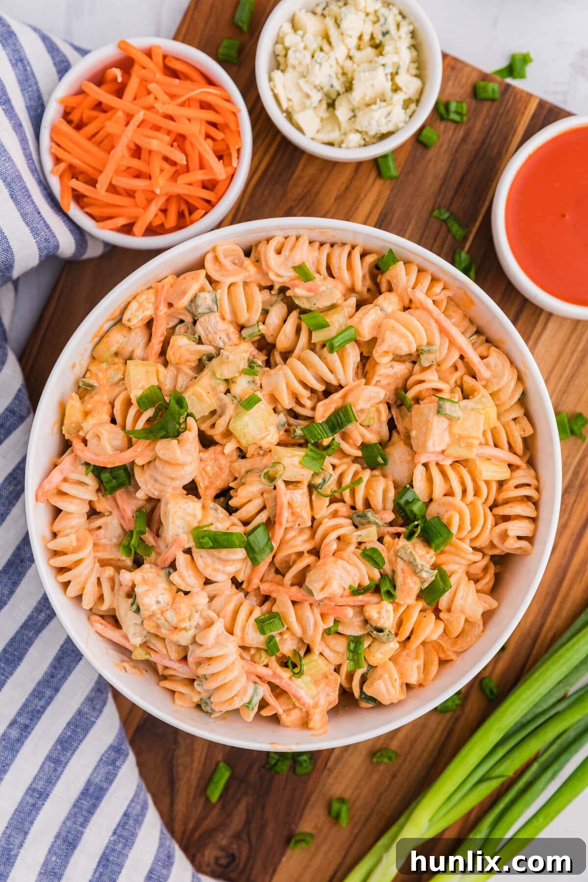 A bowl of Buffalo Chicken Pasta Salad on a wooden cutting board surrounded by ingredients.