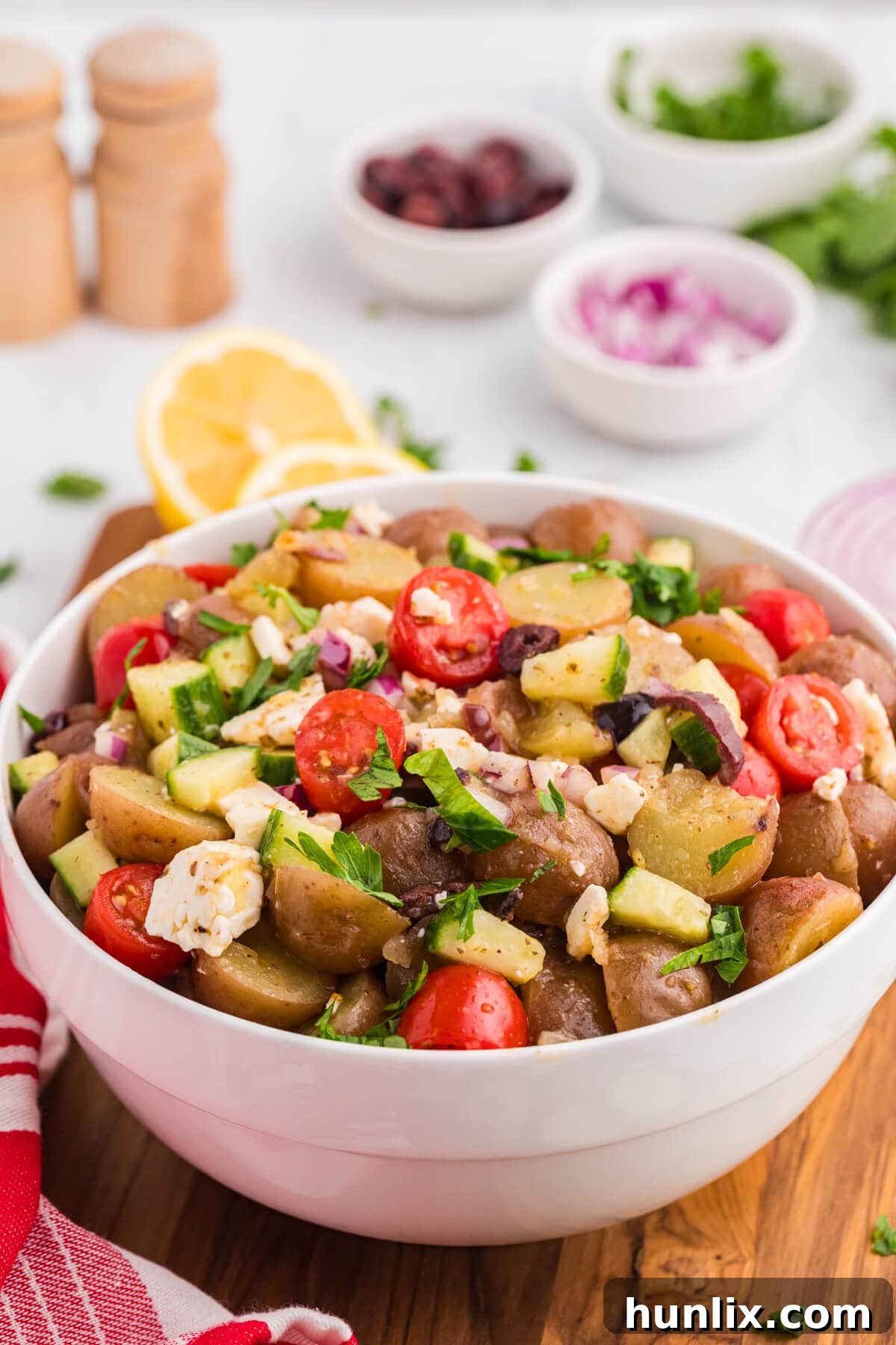 A crisp, vibrant white bowl filled with Greek Potato Salad, showcasing its colorful medley of ingredients and light dressing.