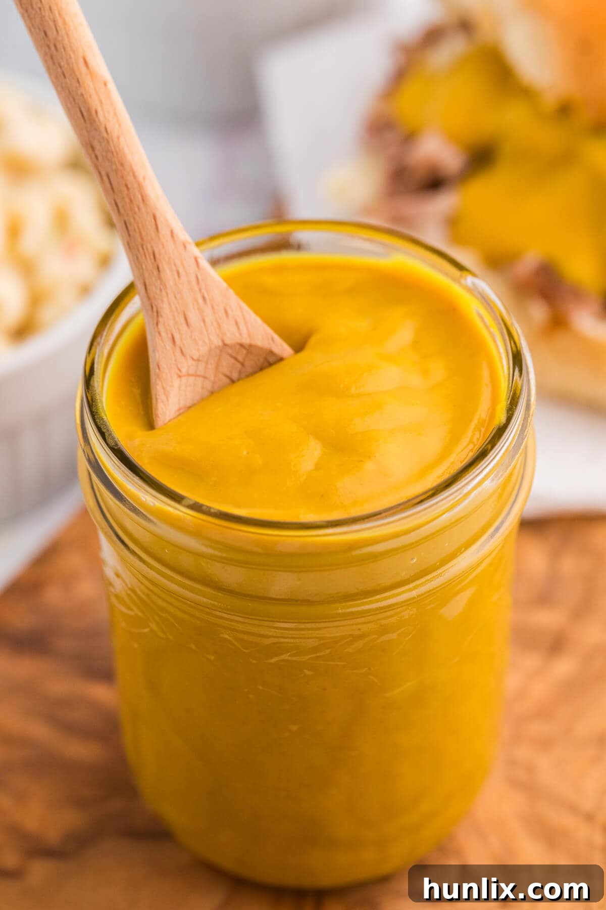 A charming close-up of the Carolina Mustard BBQ Sauce in a glass jar, with a wooden spoon resting inside.