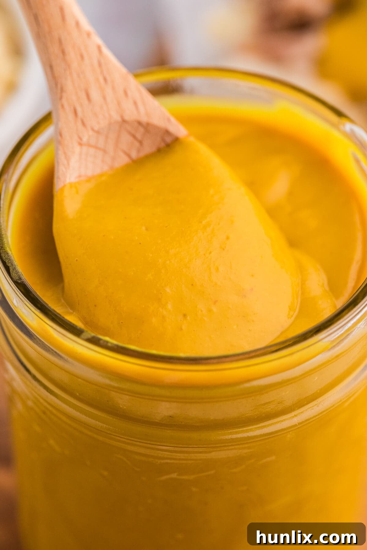 A wooden spoon scooping a generous amount of Carolina Mustard BBQ Sauce from a glass jar.