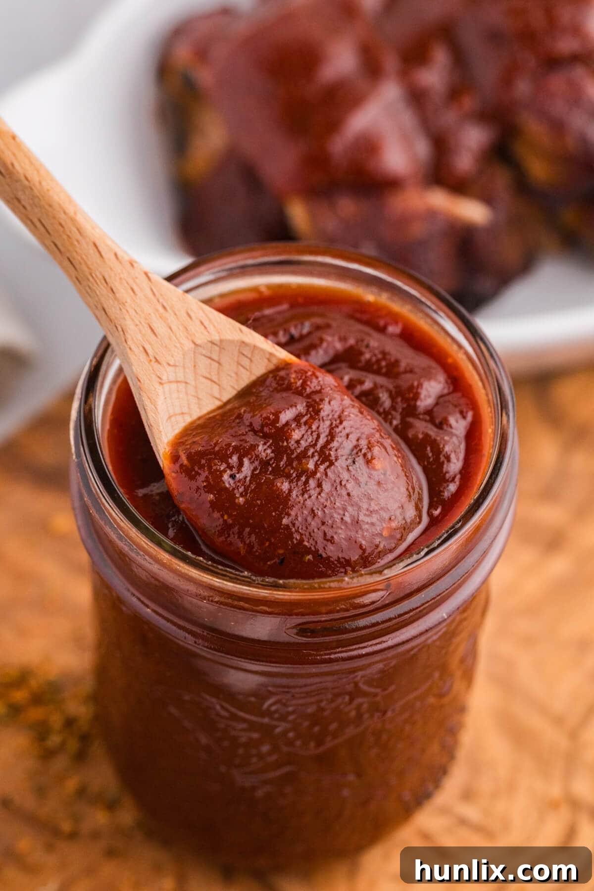 A wooden spoon scooping thick Cajun BBQ Sauce from a glass jar.