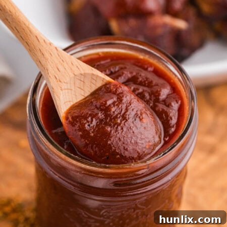 The finished Cajun BBQ Sauce in a jar with a wooden spoon.