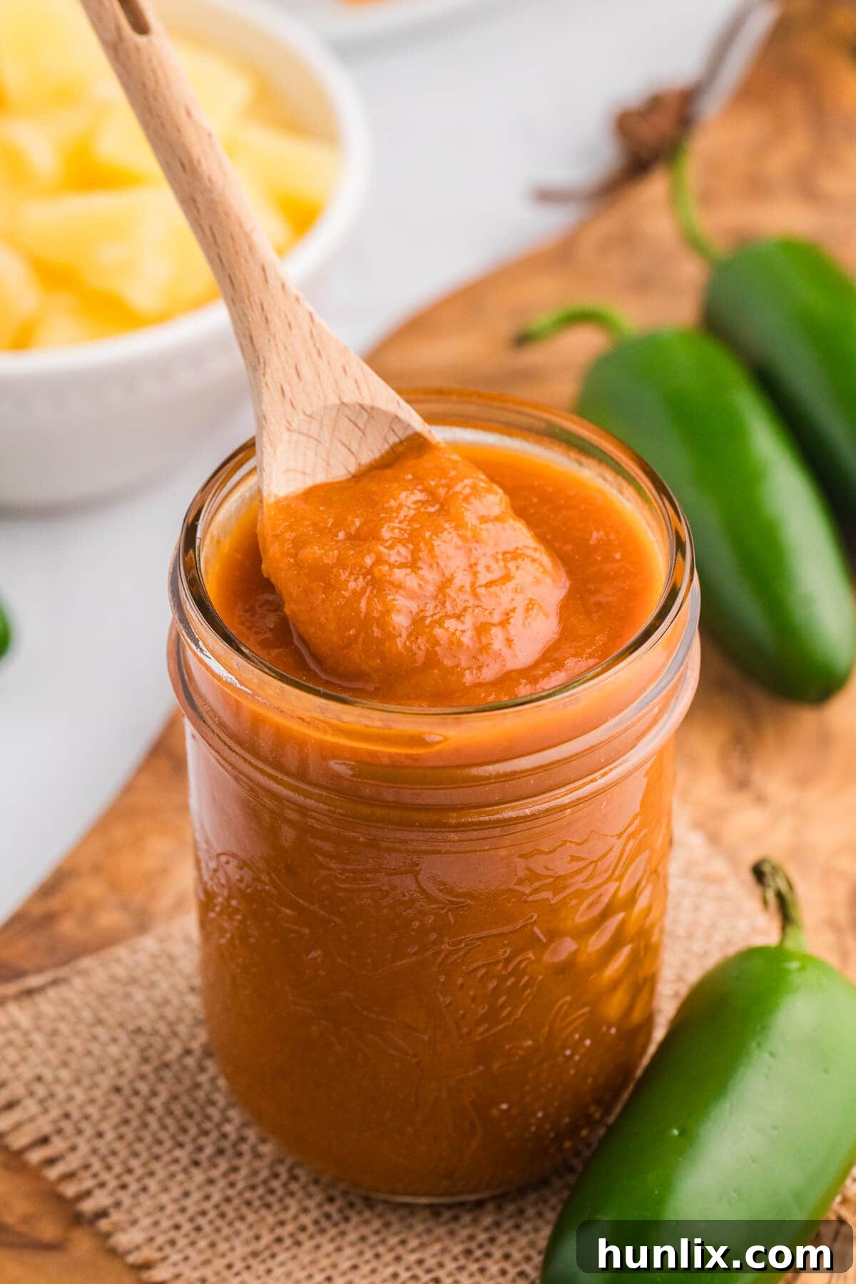 Sweet Heat Pineapple Jalapeno BBQ 5 Pineapple Jalapeño BBQ Sauce in a jar with a wooden spoon and a chicken platter.