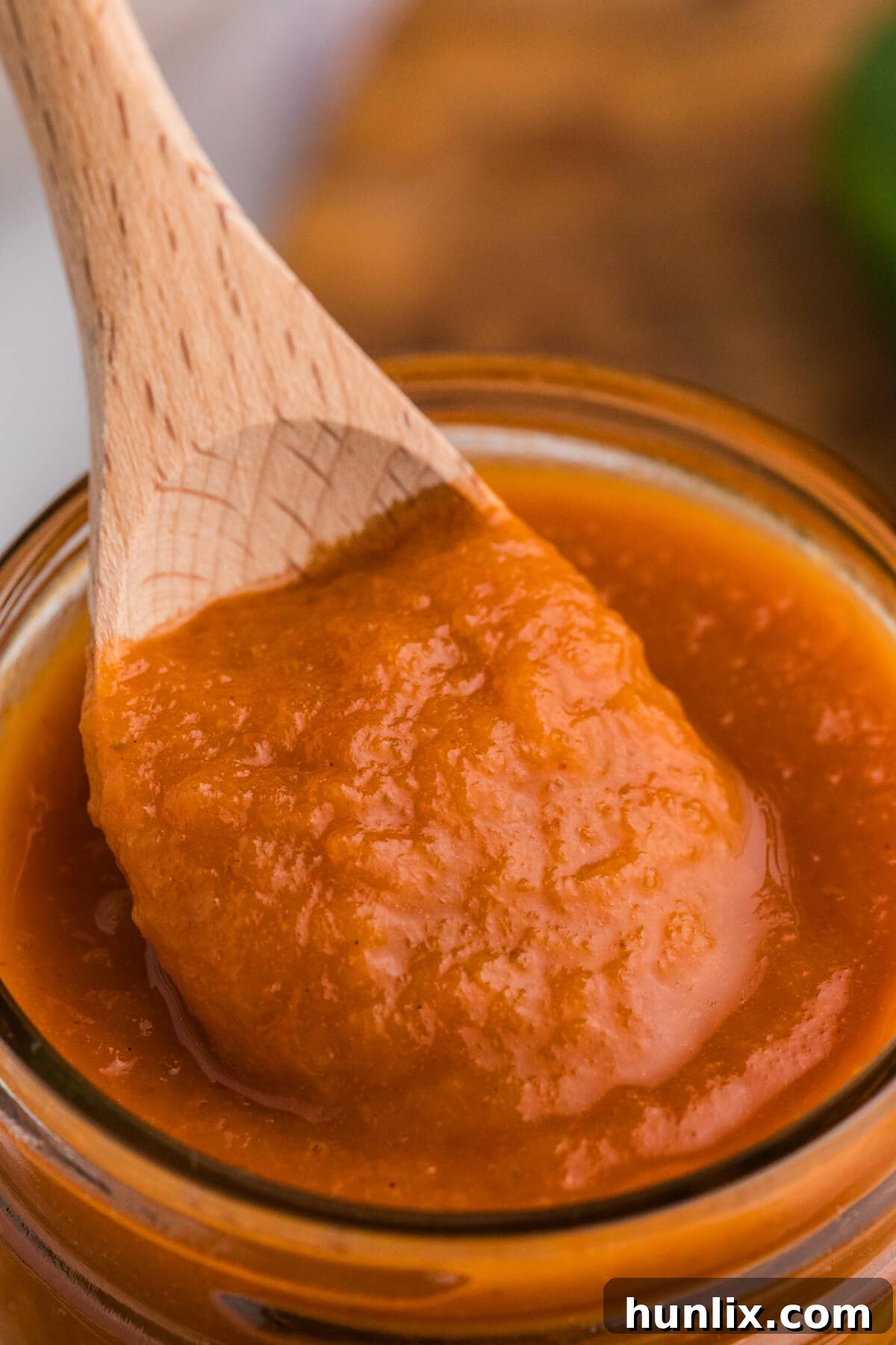 Sweet Heat Pineapple Jalapeno BBQ 6 Pineapple Jalapeño BBQ Sauce on a wooden spoon, taken from a jar.