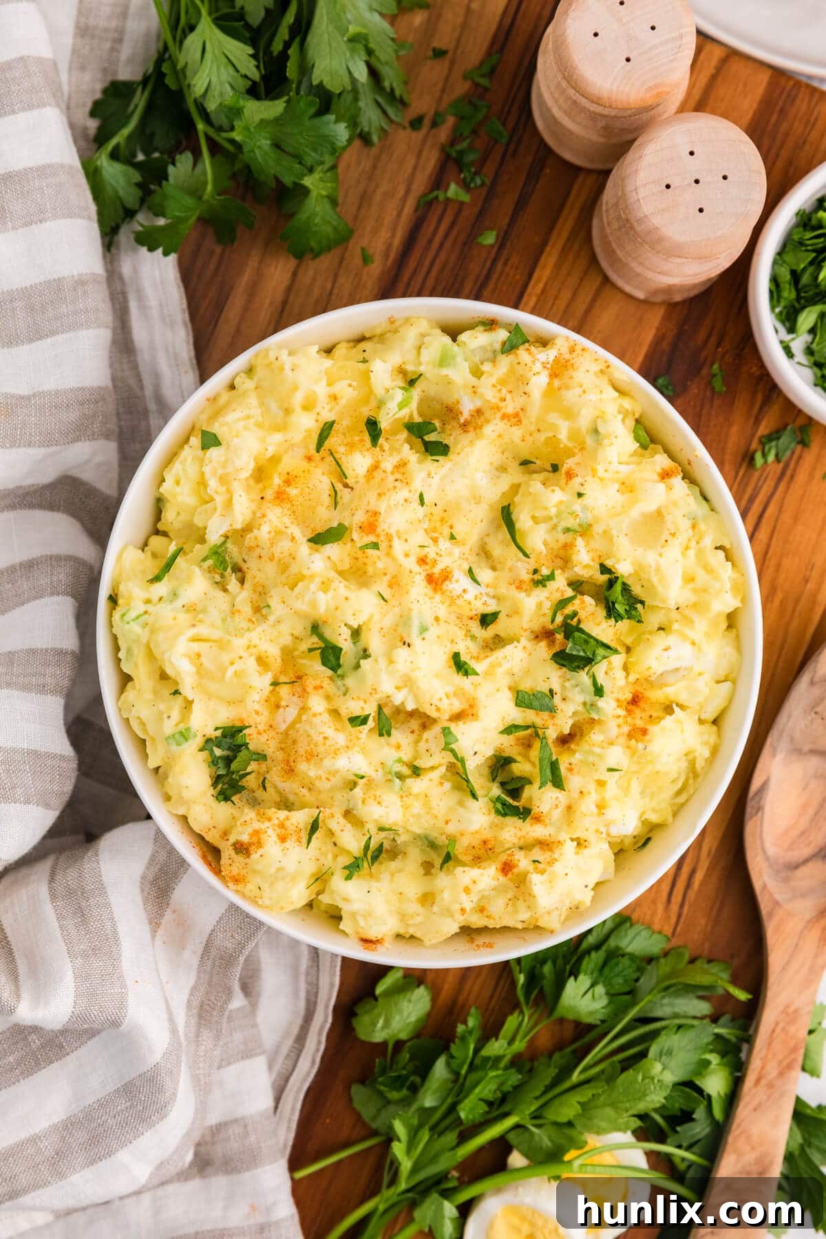 A beautifully presented bowl of creamy Old-Fashioned Potato Salad, garnished with a sprinkle of paprika and fresh parsley, sitting on a rustic wooden surface, ready to be served.