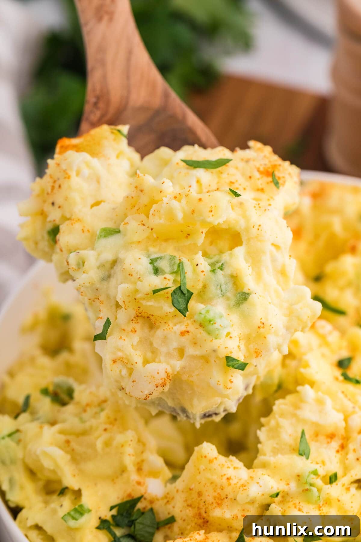 A close-up shot of a creamy spoonful of Old-Fashioned Potato Salad, highlighting its inviting texture and the finely chopped ingredients within. The background is softly blurred.