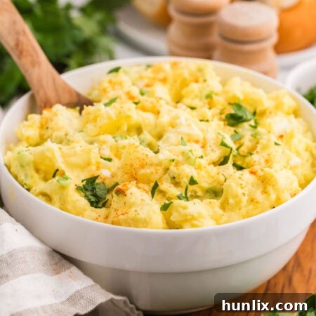 The finished Old-Fashioned Potato Salad in a white bowl with a wooden spoon, ready to be served.