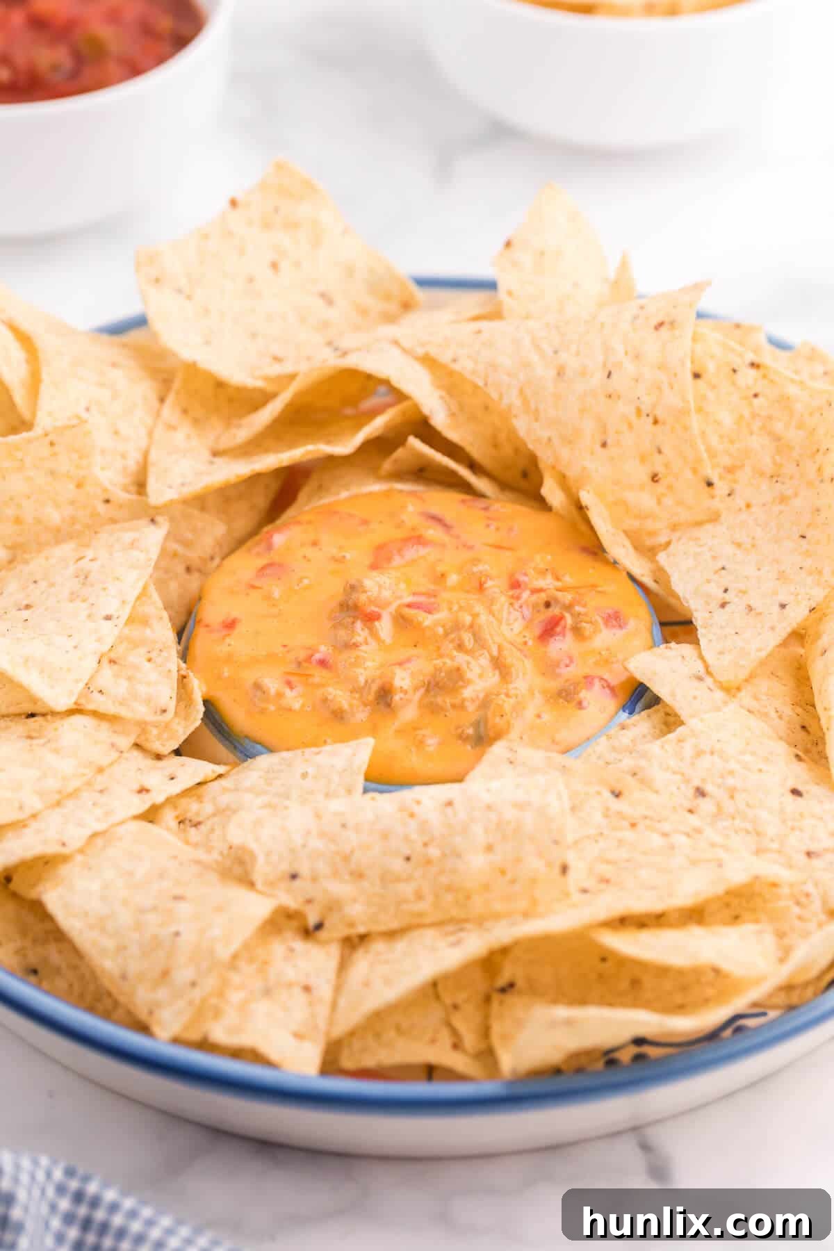 The Hot Dips You Won't Believe You Lived Without 11 A bowl of creamy Chicken Queso Dip with tortilla chips ready for dipping, garnished with a sprinkle of cilantro.