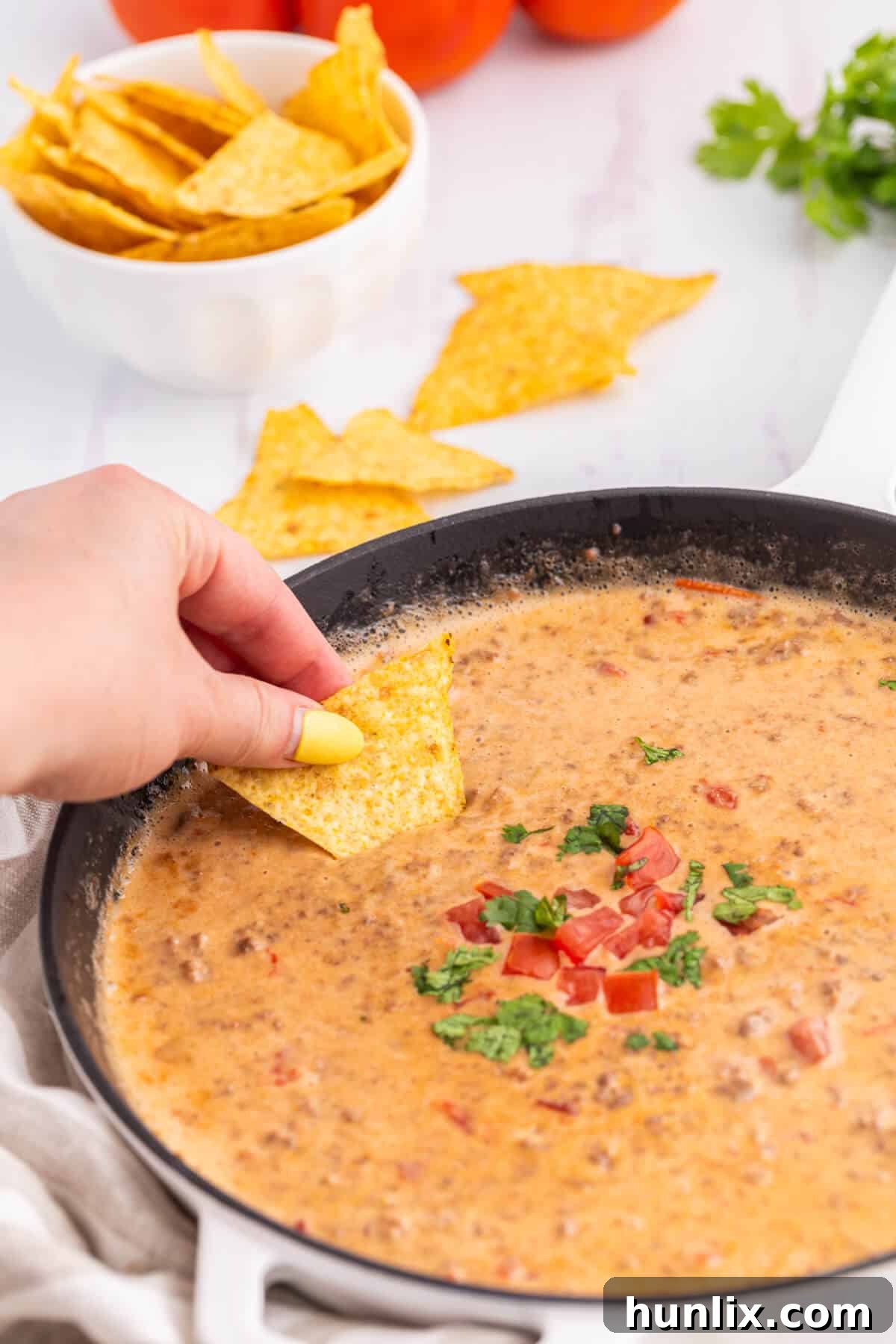 The Hot Dips You Won't Believe You Lived Without 5 Close-up of a bubbling Rotel Dip with ground beef and melted cheese, garnished with a sprig of cilantro.