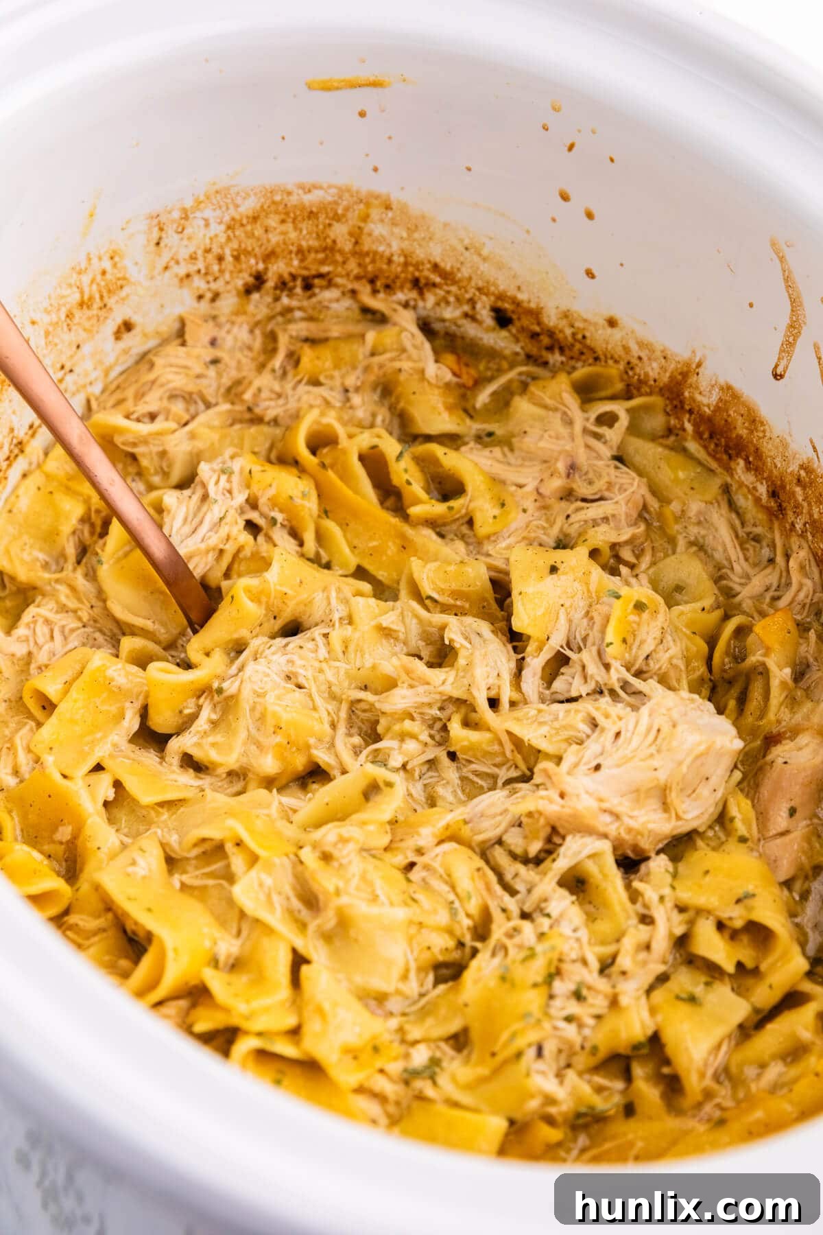 The recipe in a white Crockpot with a serving spoon, showcasing a creamy and comforting Slow Cooker Chicken and Noodles dish.