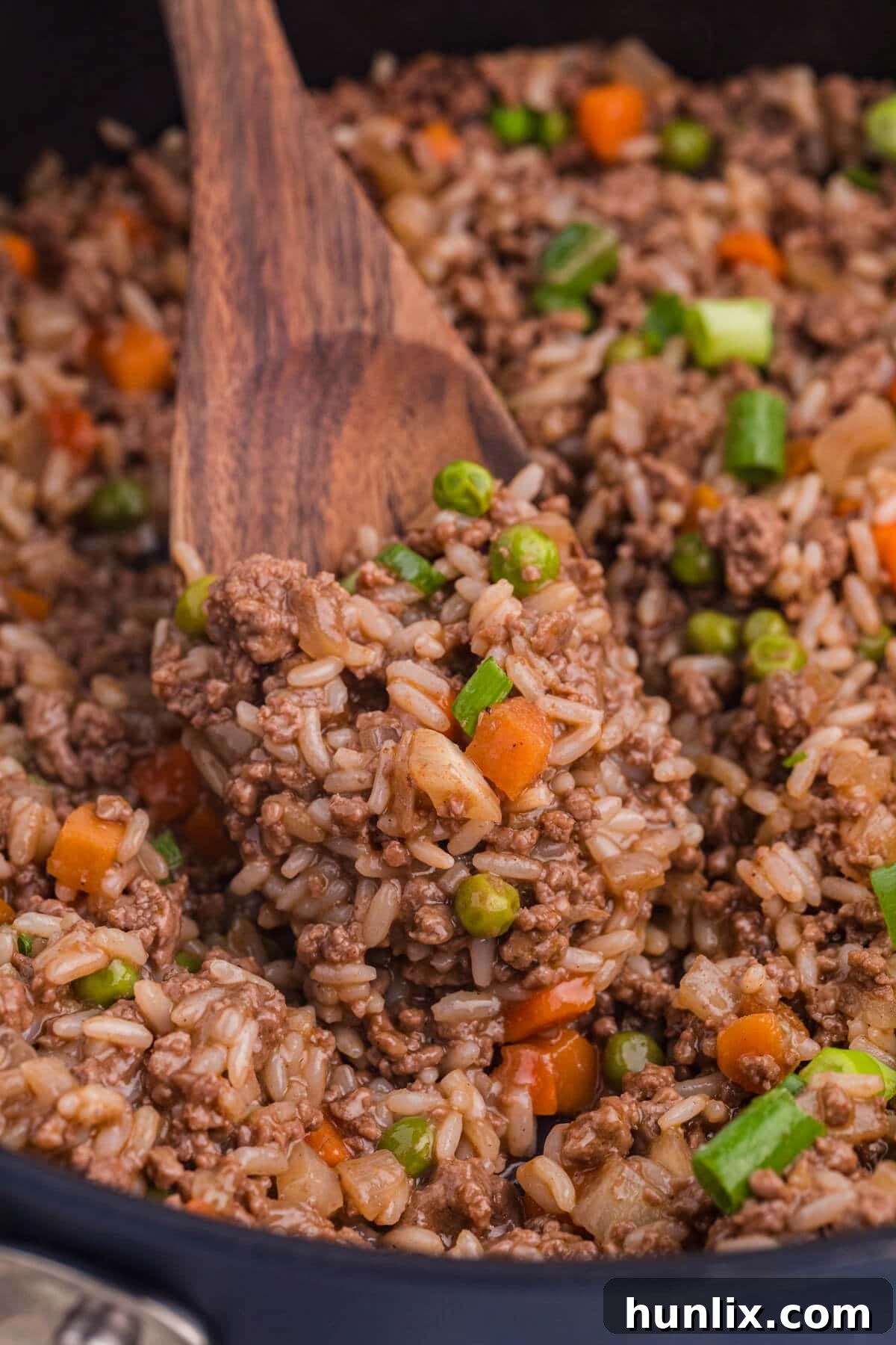 Easy Skillet BBQ Beef and Rice 6 A wooden spoon scooping a portion of the BBQ beef and rice from the skillet, showcasing the texture.