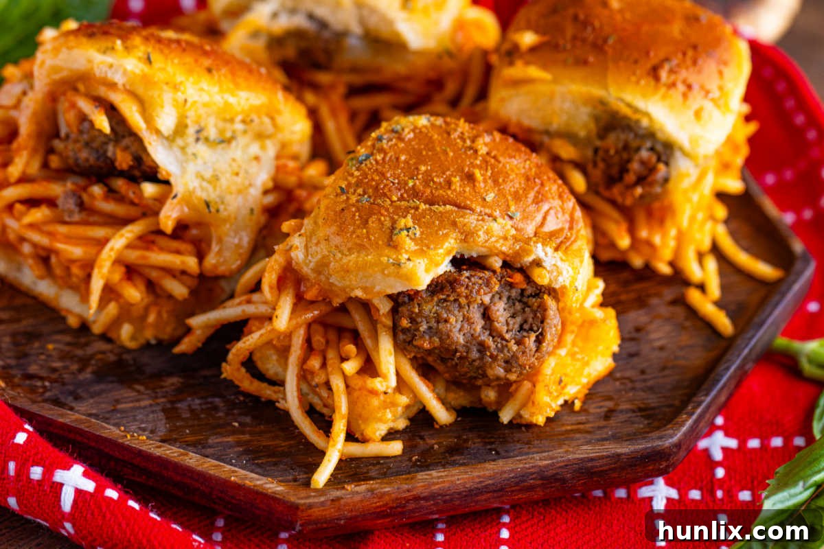 Spaghetti and meatball sliders on a wooden platter, garnished with fresh herbs.