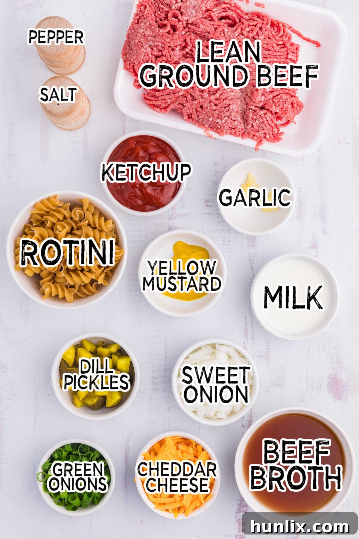 Assorted ingredients laid out on a white background, including ground beef, pasta, cheese, and condiments, ready for cooking.