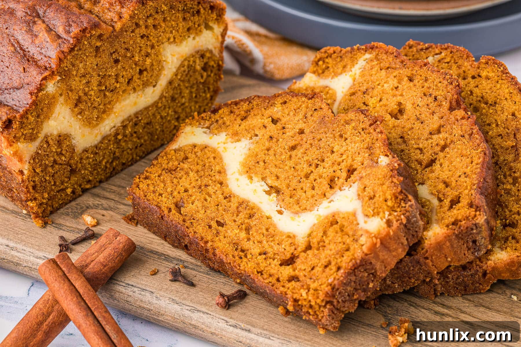 Slices of moist Pumpkin Ribbon Bread with a creamy cheesecake swirl, displayed on a wooden cutting board.
