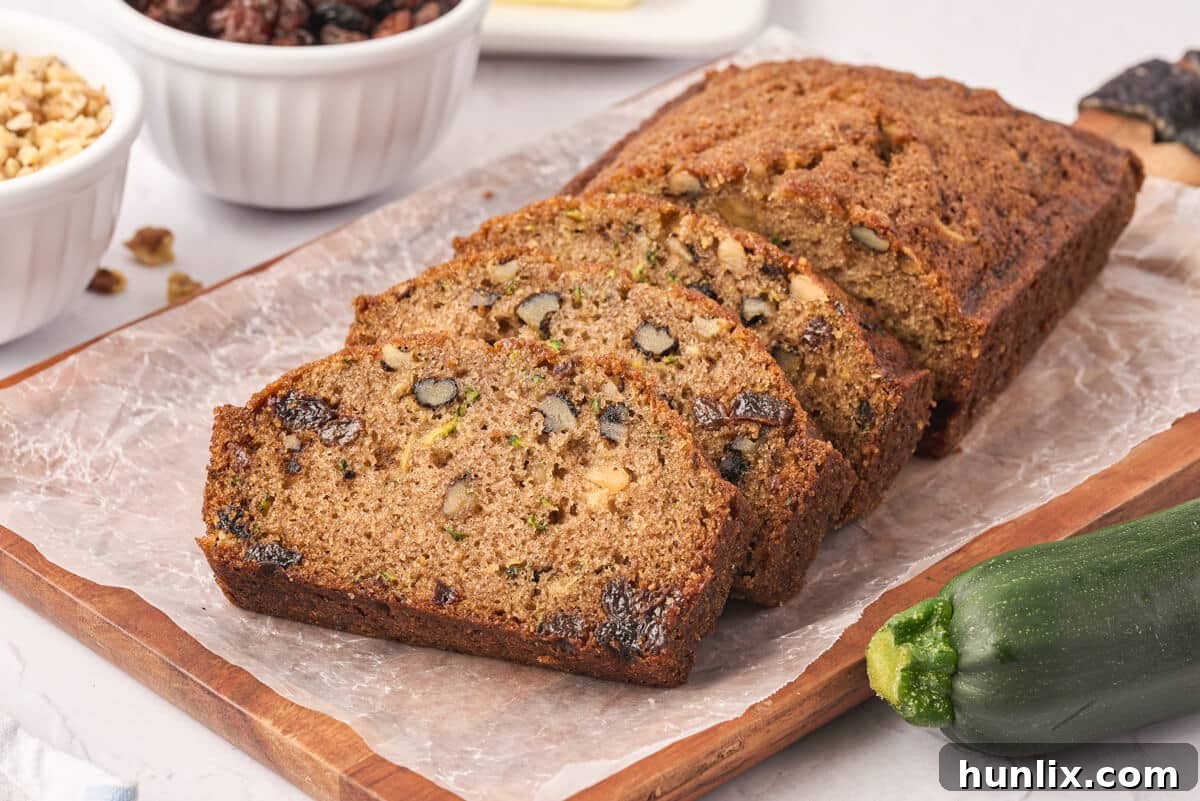 Slices of moist zucchini bread with nuts and raisins on a cutting board.