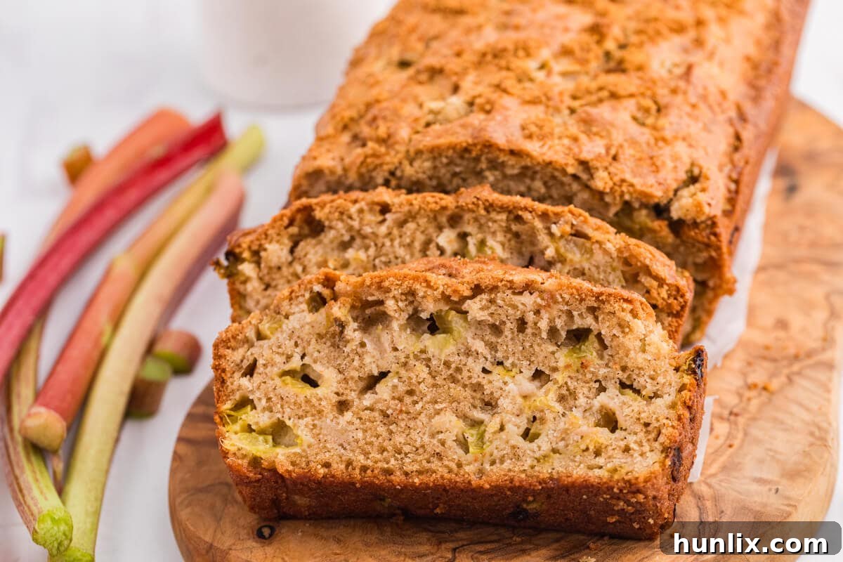 A beautifully baked loaf of Rhubarb Bread on a cutting board, ready to be sliced.