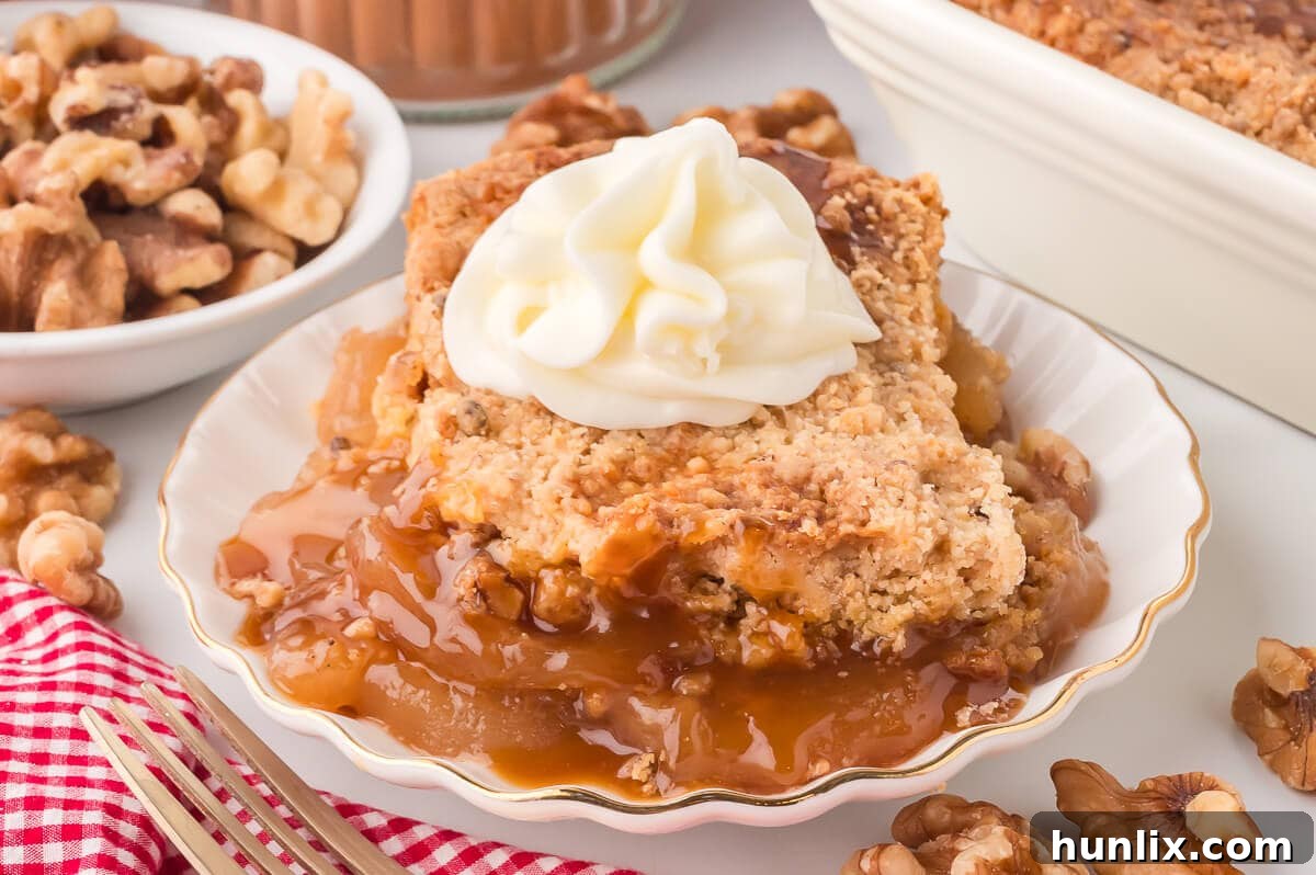 A delectable slice of Apple Dump Cake on a white plate, elegantly topped with a swirl of light whipped cream.