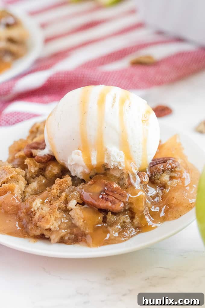 A generous slice of Caramel Apple Dump Cake on a white plate, accompanied by a scoop of creamy vanilla ice cream, highlighting its inviting layers.