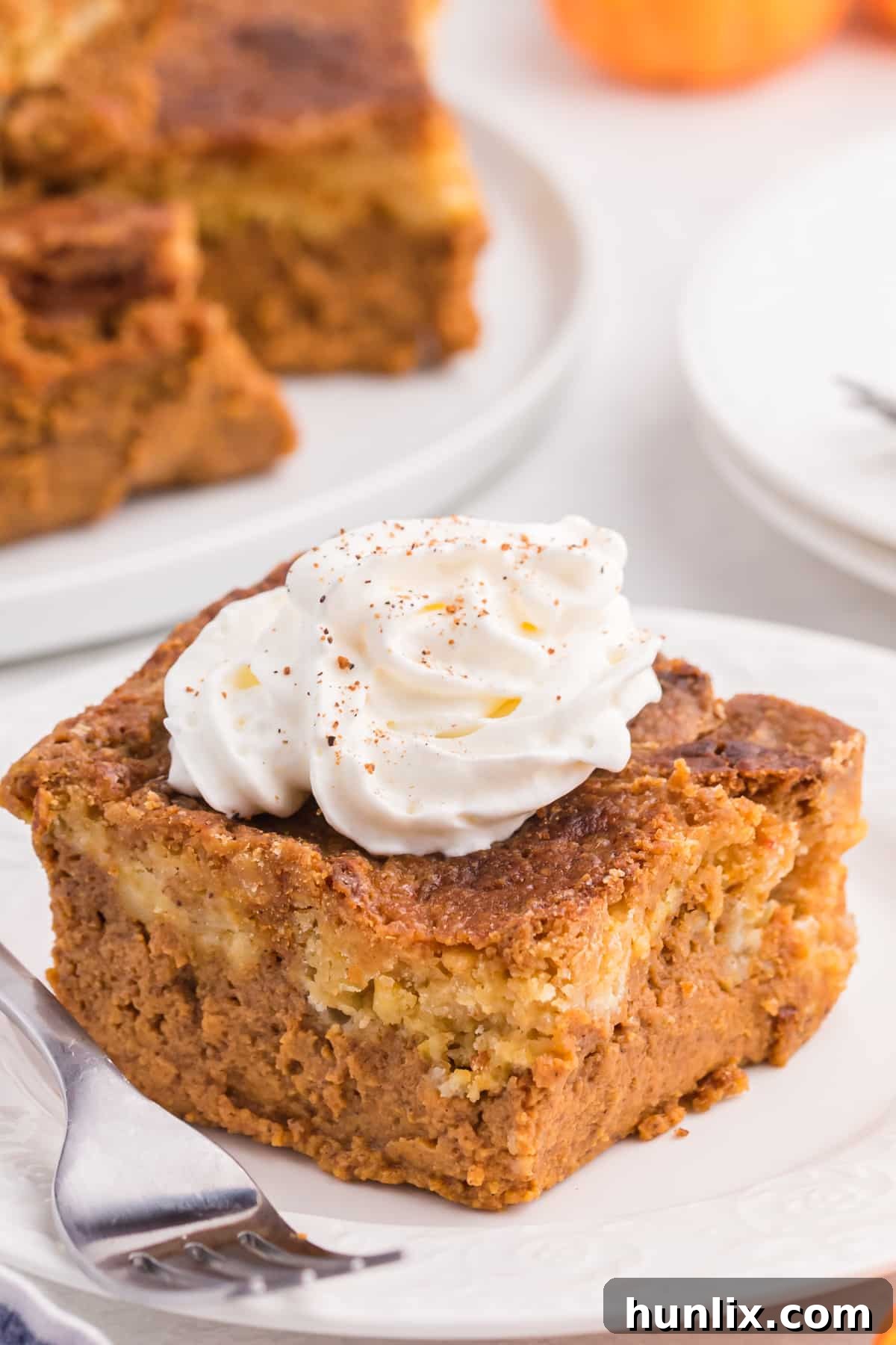 A tempting slice of Pumpkin Dump Cake, elegantly topped with a swirl of light whipped cream, ready for a delicious autumn treat.