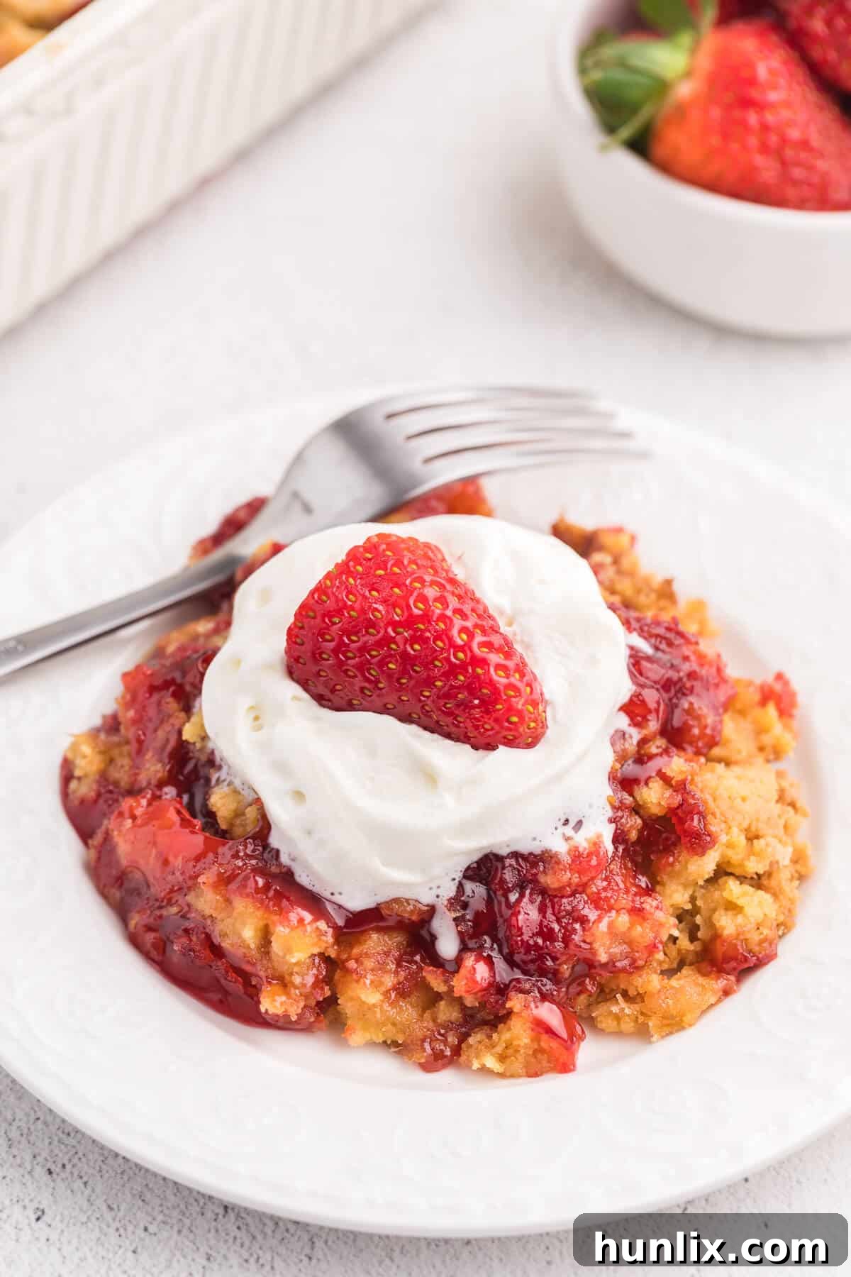 A inviting slice of Strawberry Dump Cake on a white plate, with a fork poised, highlighting its tender, fruity layers.