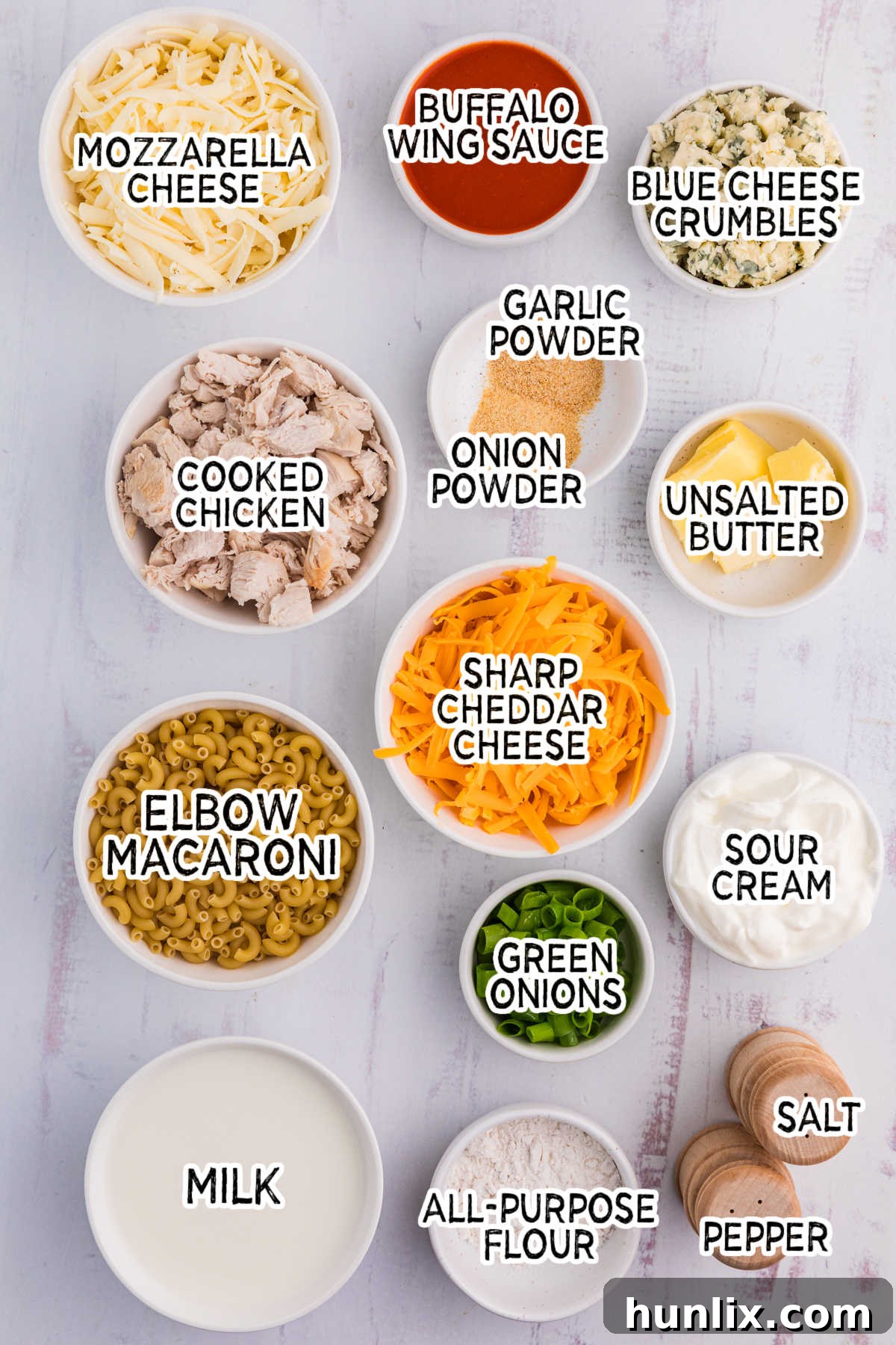 A vibrant assortment of Buffalo Chicken Mac and Cheese ingredients, including elbow macaroni, various cheeses, butter, and buffalo sauce, artfully arranged on a clean white surface.