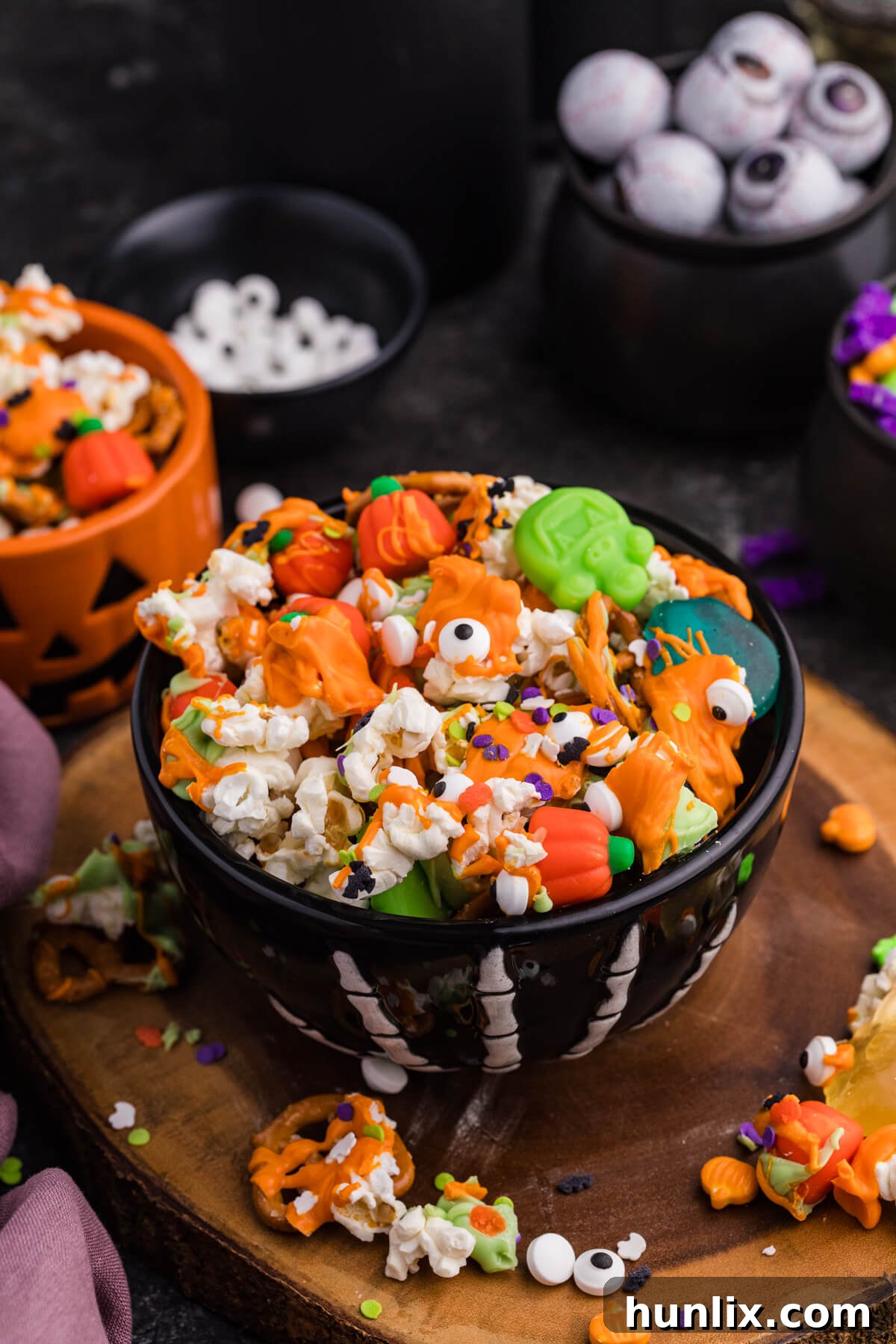 Spooky Halloween Popcorn 2 A vibrant bowl of Halloween Popcorn featuring green gummy monsters, mellowcreme pumpkins, sprinkles, and candy eyeballs, set against a spooky Halloween backdrop.