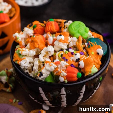 Spooky Halloween Popcorn 7 Black skeleton bowl filled with Halloween Popcorn, topped with orange and green candy melt drizzle, pretzels, mellowcreme pumpkins, and candy eyeballs.