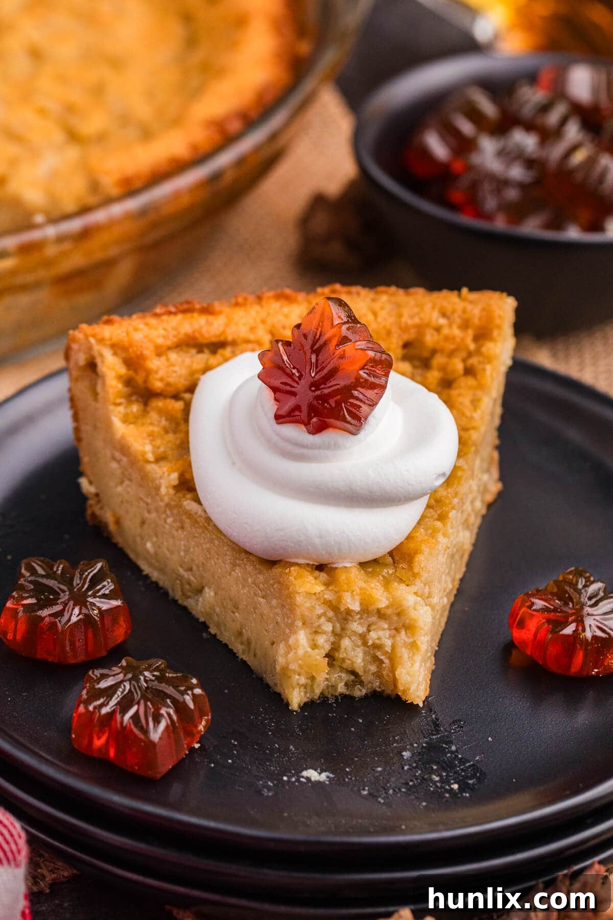 Maple Magic Pie 7 A close-up shot of a slice of Maple Impossible Pie, garnished with whipped cream and two small decorative maple leaf candies, on a rustic plate.
