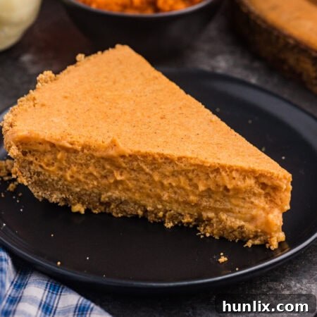 A plain slice of chilled pumpkin pie with a graham cracker crust sits on a black plate with pumpkins and a bowl of pumpkin purée in the background.