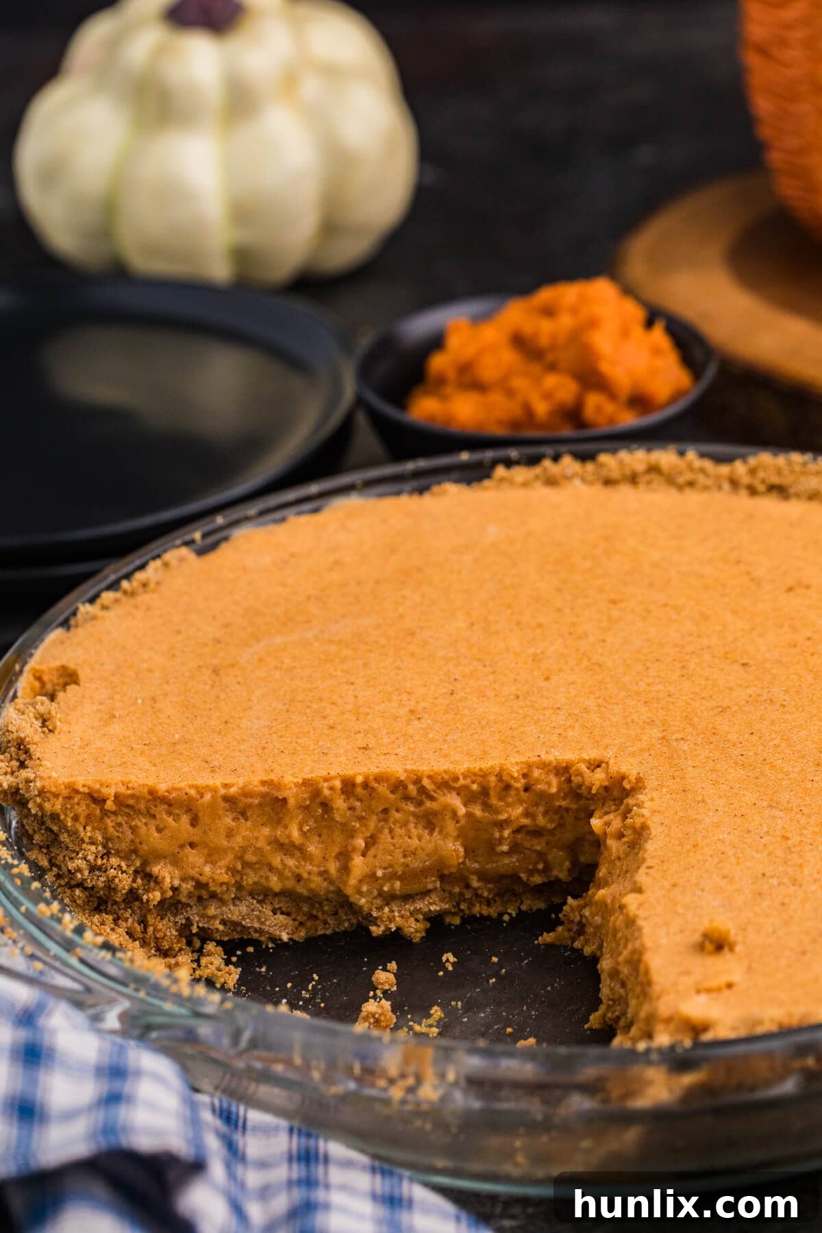 Whipped Pumpkin Delight 9 A partially sliced creamy pumpkin pie sits in a glass pie dish with a graham cracker crust, with pumpkins and a bowl of pumpkin purée in the background.