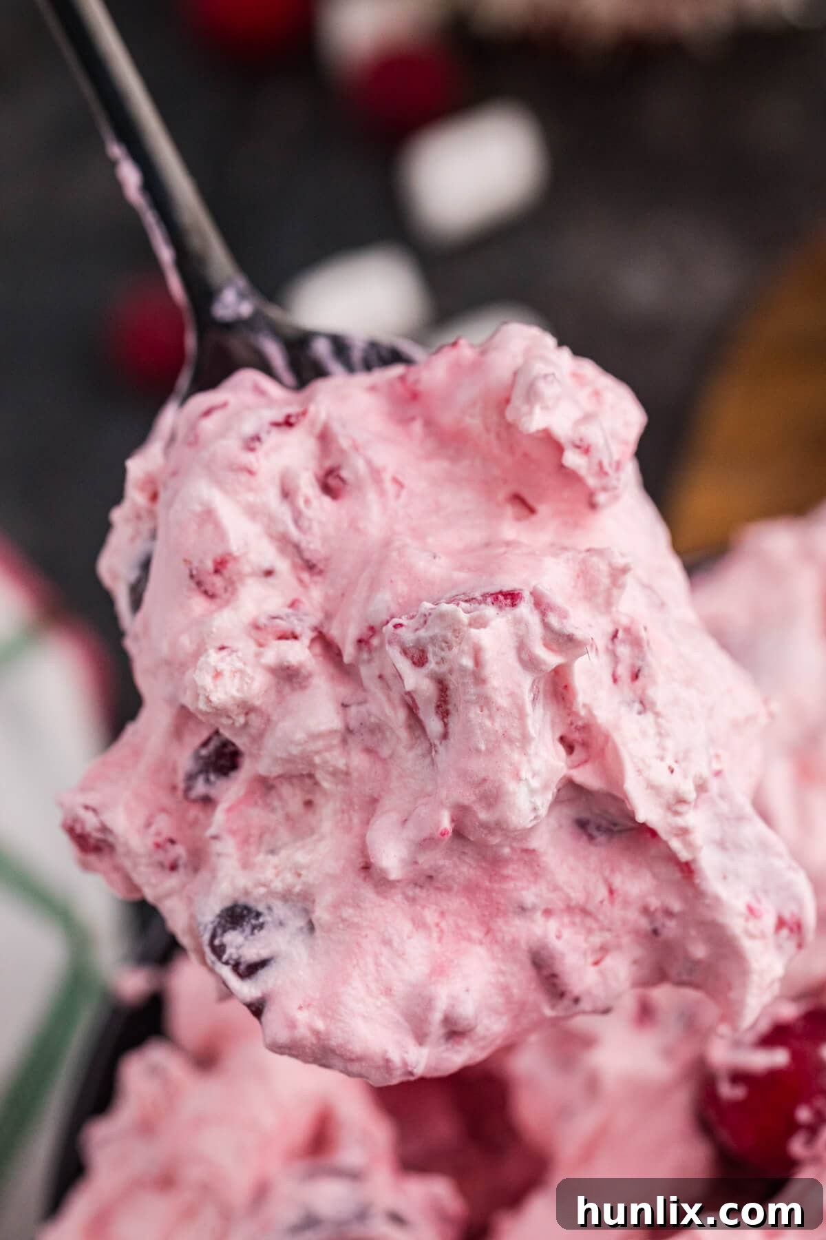A close-up shot of a spoonful of fluffy pink dessert, showcasing its creamy texture with visible chunks of cranberries and soft marshmallows, highlighting the deliciousness and festive ingredients.
