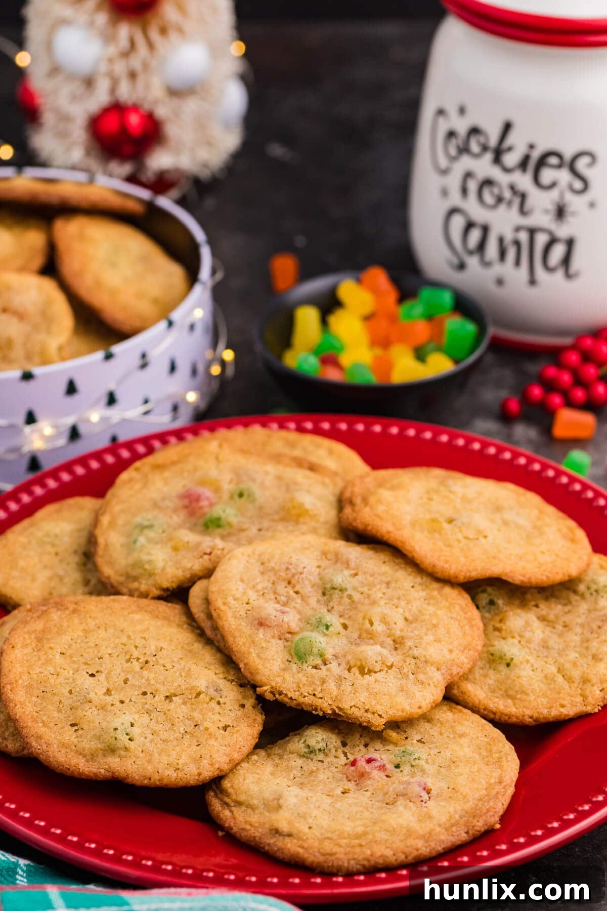 Festive Gumdrop Gems 2 Gumdrop cookies on a red plate, studded with colorful candy pieces, surrounded by festive Christmas decor and a “Cookies for Santa” jar.
