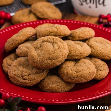 Plate of golden, sugar-coated holiday cookies stacked on a red dish, surrounded by festive decor including red berries and a “Cookies for Santa” jar in the background.