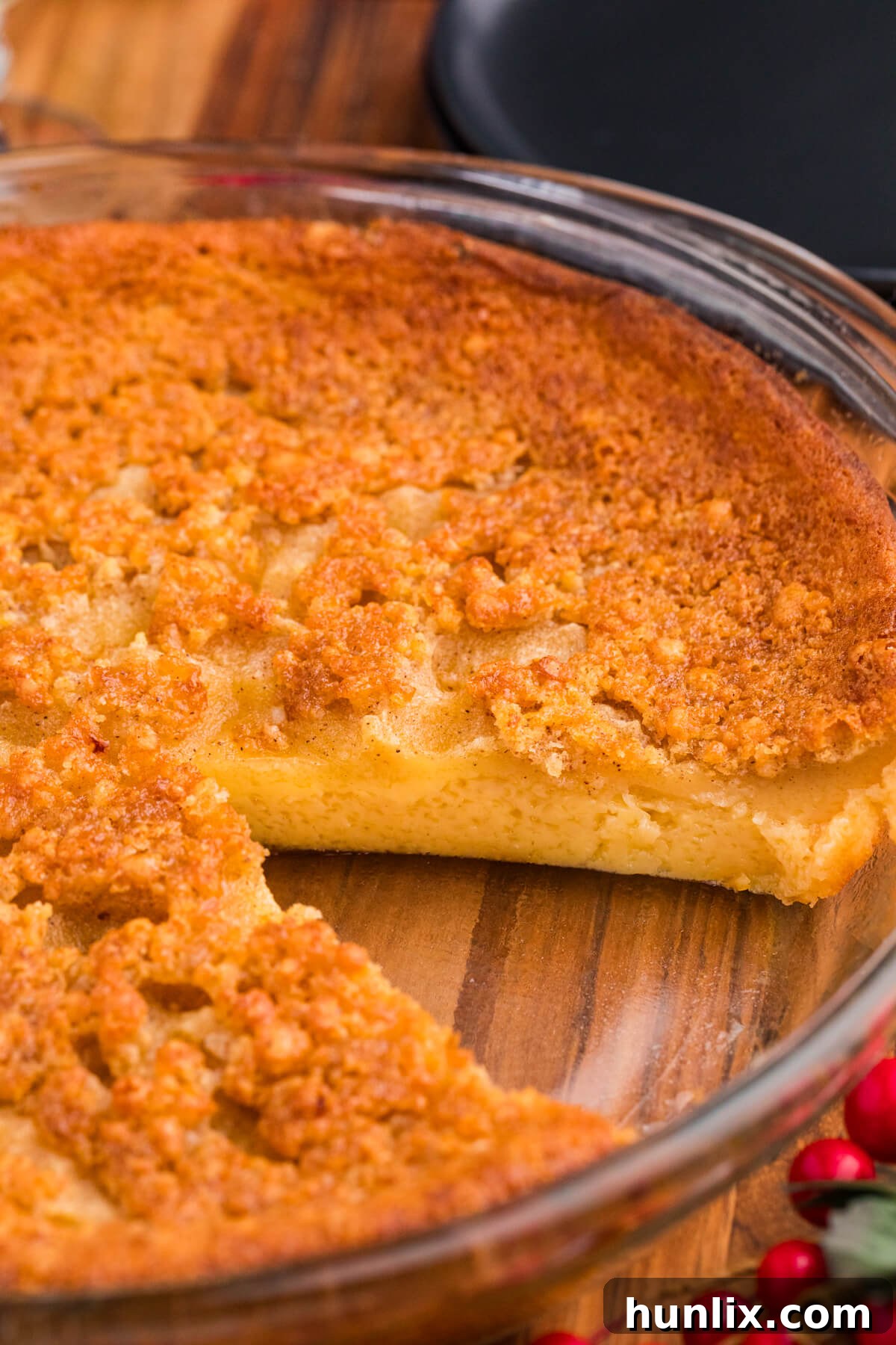 Golden brown custard pie with a creamy center in a glass dish, set on a wooden table with festive red berries nearby.