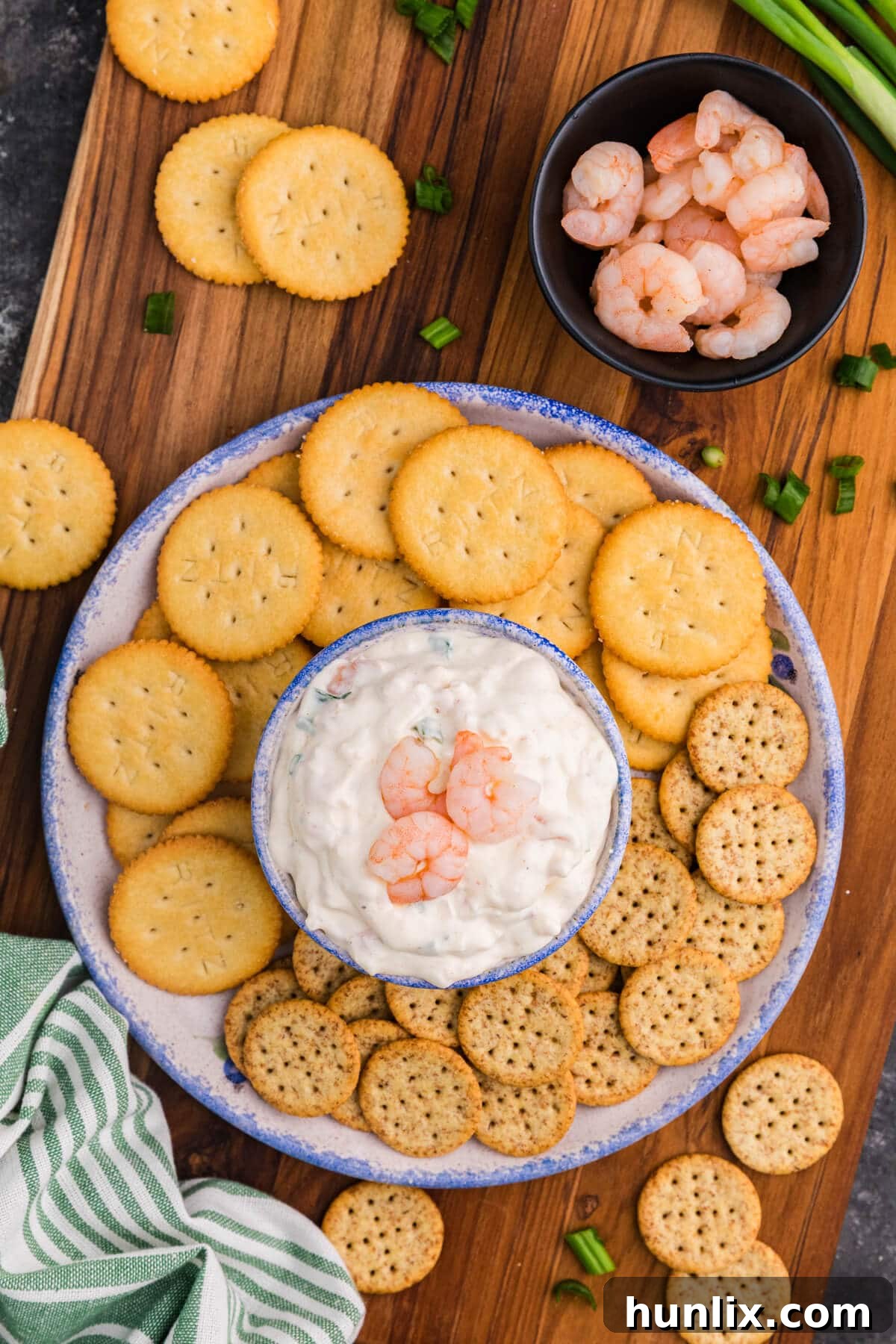 Irresistible Shrimp Dip 2 Shrimp Dip in a ceramic bowl topped with whole shrimp, surrounded by Ritz and multigrain crackers on a wooden board with green onions and a bowl of shrimp.