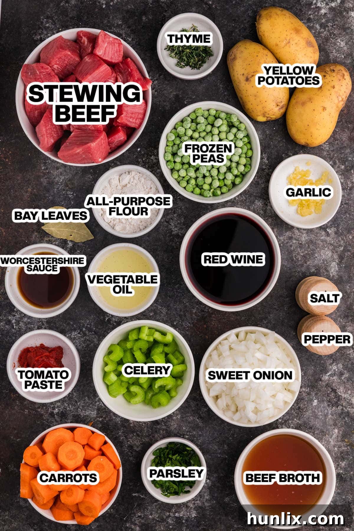 A beautifully arranged flat lay of all the essential ingredients for classic beef stew, including raw beef chunks, fresh vegetables like carrots, potatoes, onions, and celery, along with herbs, spices, and liquids, set against a dark background.