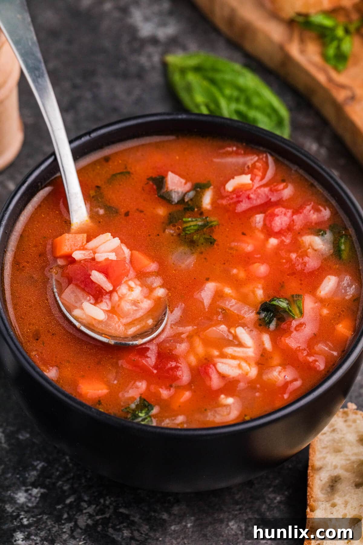 A spoon lifting a hearty scoop of tomato rice soup from a bowl, showcasing the tender rice, vegetables, and rich broth, garnished with fresh basil leaves.