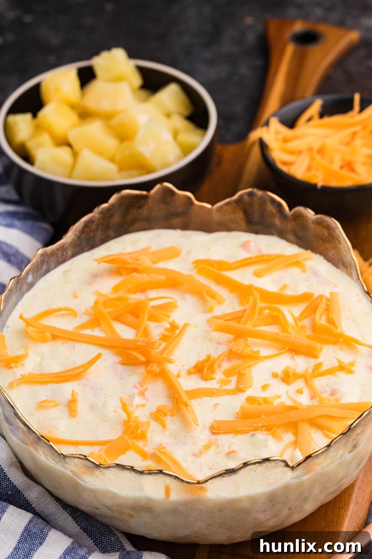 Tropical Pineapple Delight 2 Pineapple salad topped with shredded cheddar cheese, served in a decorative glass bowl, with small bowls of pineapple chunks and grated cheese in the background on a wooden board.
