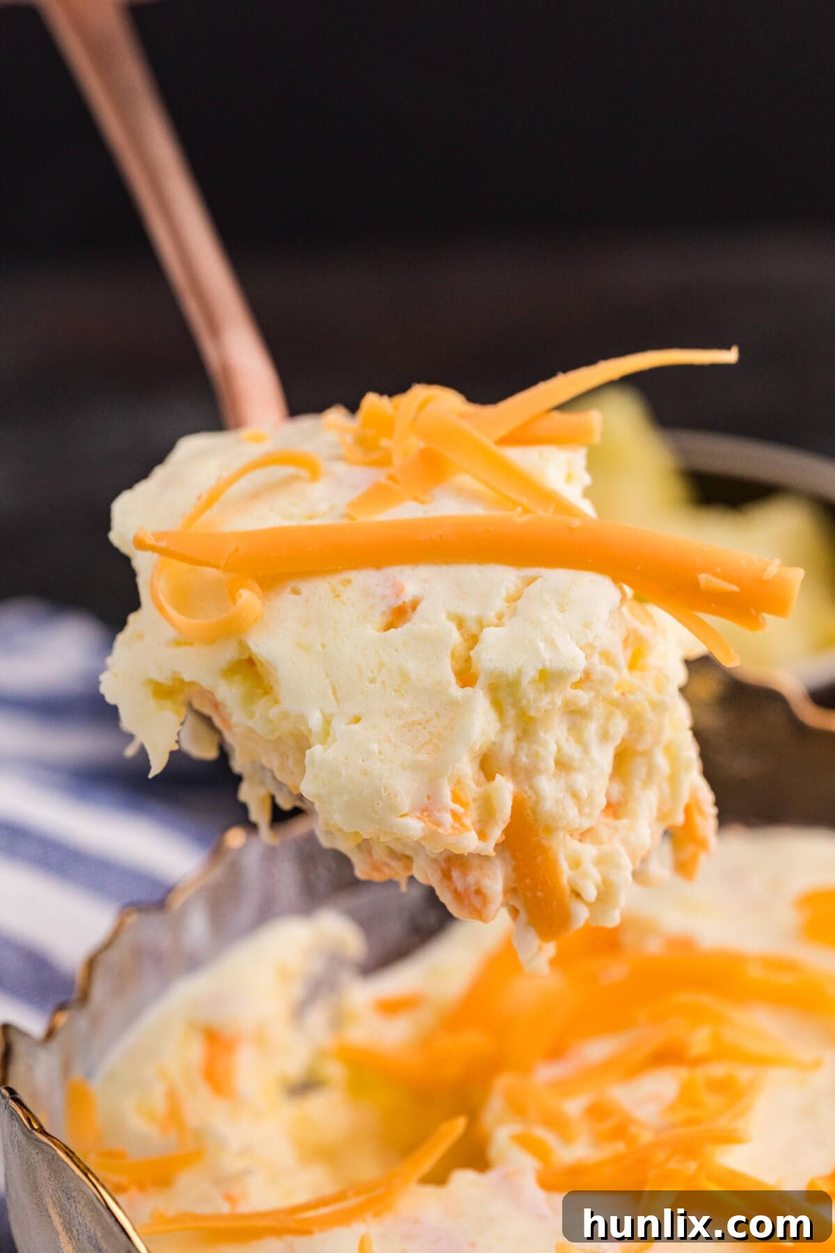 Tropical Pineapple Delight 5 Close-up of a spoonful of creamy fruit salad with visible pineapple chunks and shredded cheddar cheese, lifted above the main serving dish.