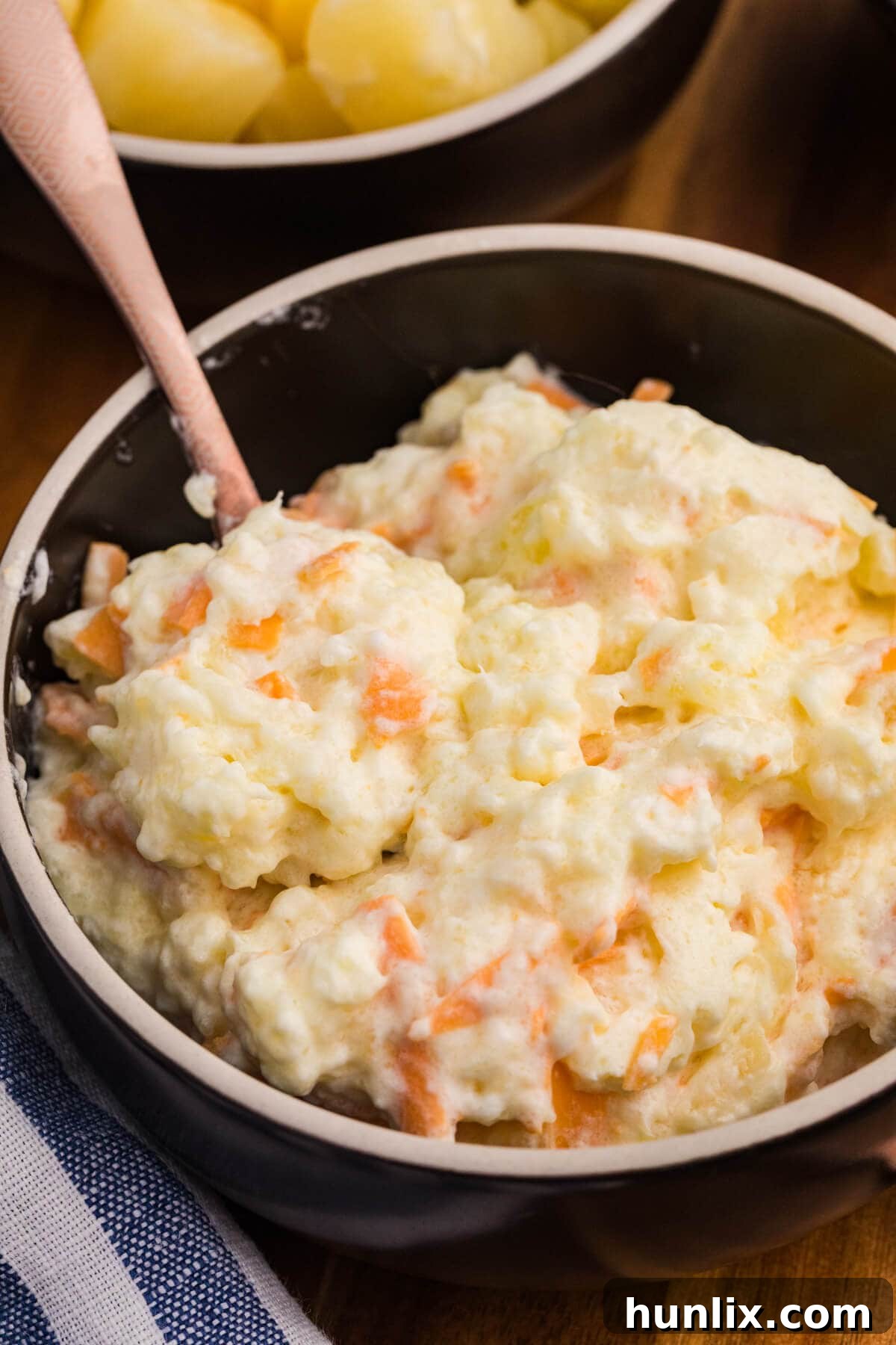 Tropical Pineapple Delight 7 Creamy fruit and cheese salad served in a black bowl, showcasing a mix of pineapple, grated carrots, and a fluffy whipped texture, with a spoon inside.