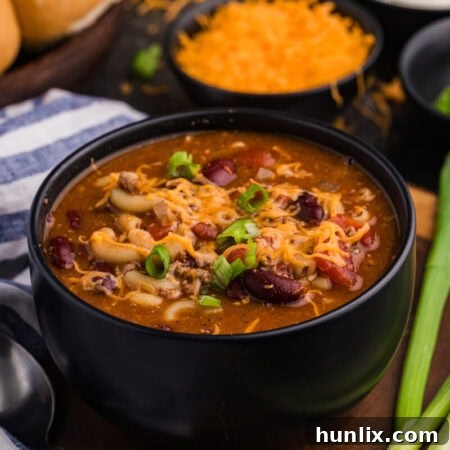 Hearty beef and bean macaroni soup in a black bowl, garnished with melted cheddar cheese and sliced green onions.