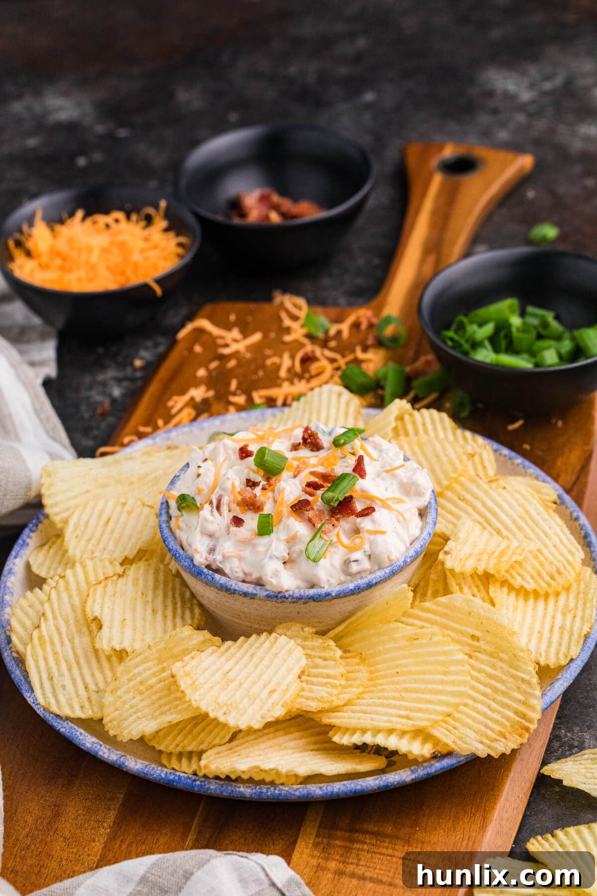 Absolutely Irresistible Dip 5 Creamy bacon cheddar ranch dip generously garnished with fresh green onions, surrounded by a vibrant array of ridged potato chips, ready for dipping.