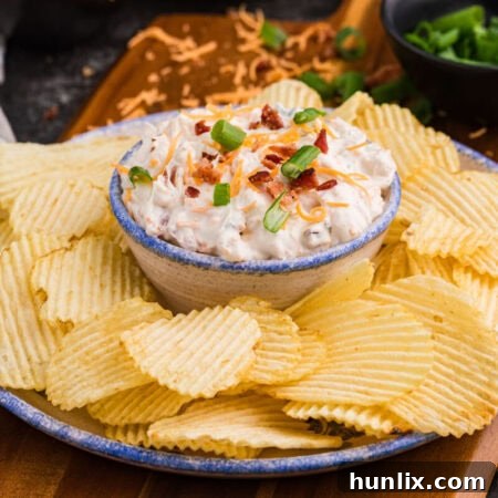 Close-up of loaded bacon cheddar dip with green onions and potato chips.