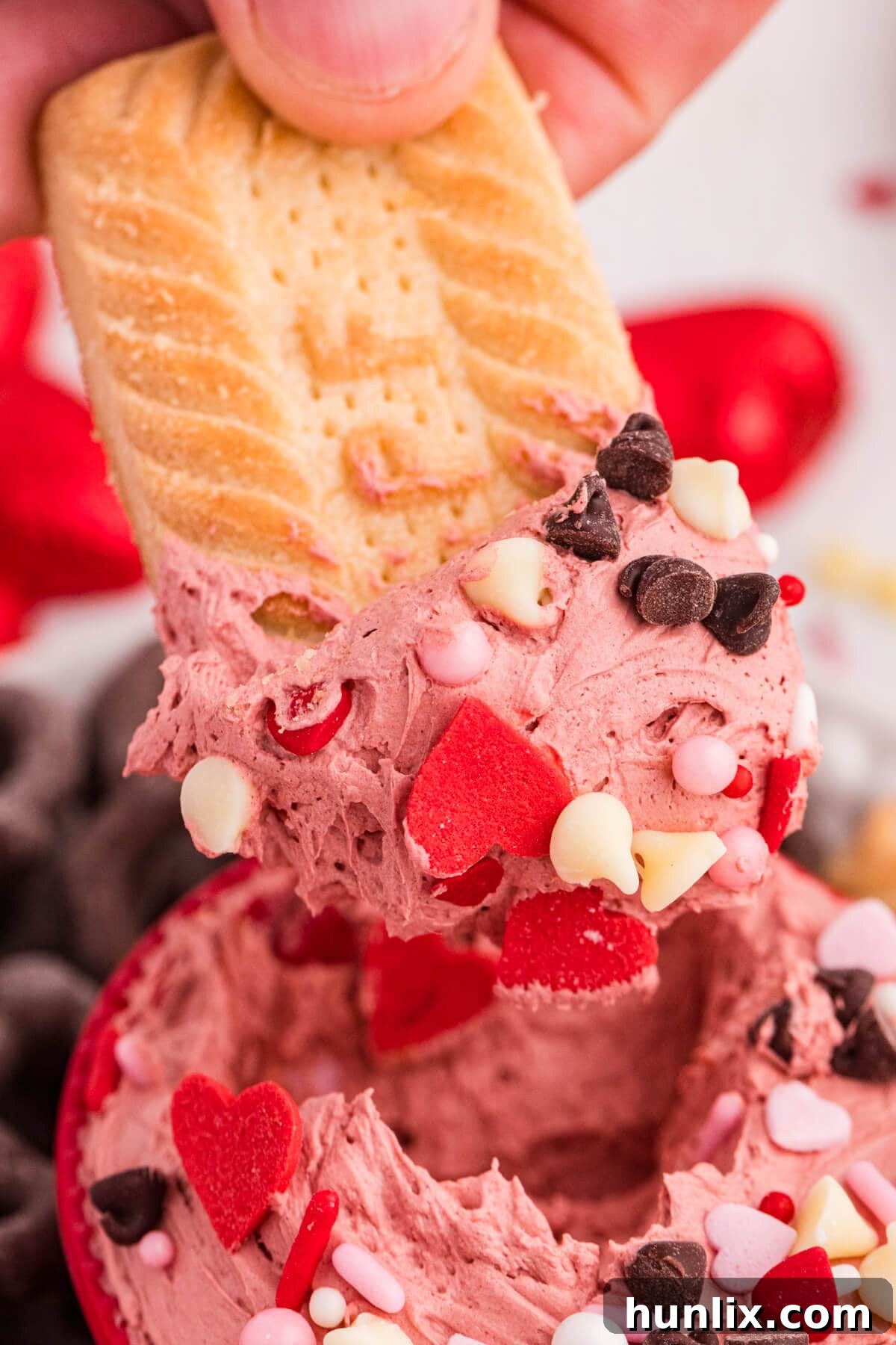 Butter cookie dipped into creamy pink cheesecake dip with heart sprinkles and chocolate chips.