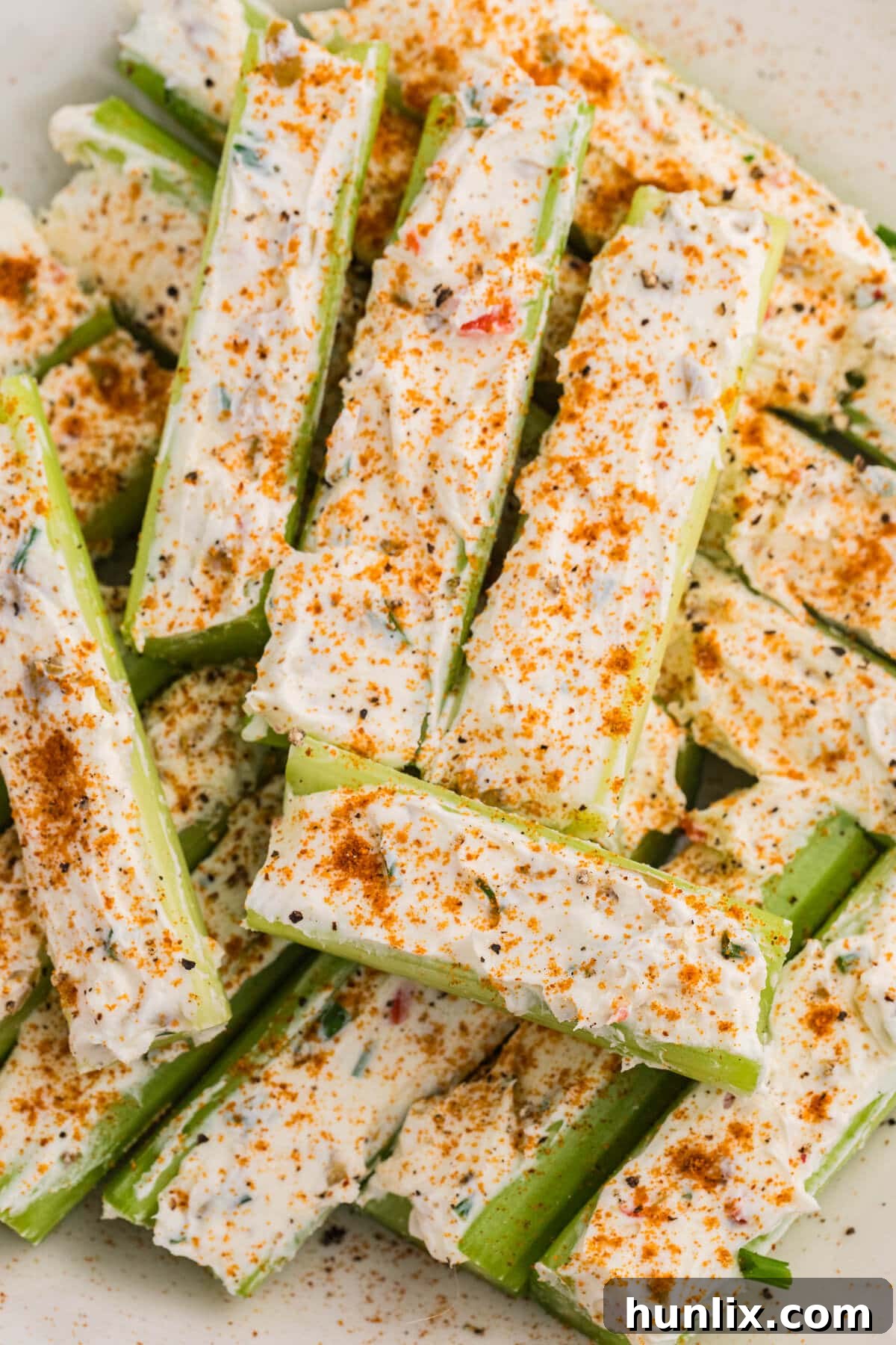 Close-up of stuffed celery filled with creamy seasoned cheese spread, garnished with paprika and herbs, highlighting the texture of the filling and crisp green celery.