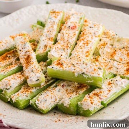 Plate of stuffed celery sticks topped with paprika seasoning and creamy cheese filling, styled with olives, carrot sticks, and fresh chives on a bright kitchen surface.