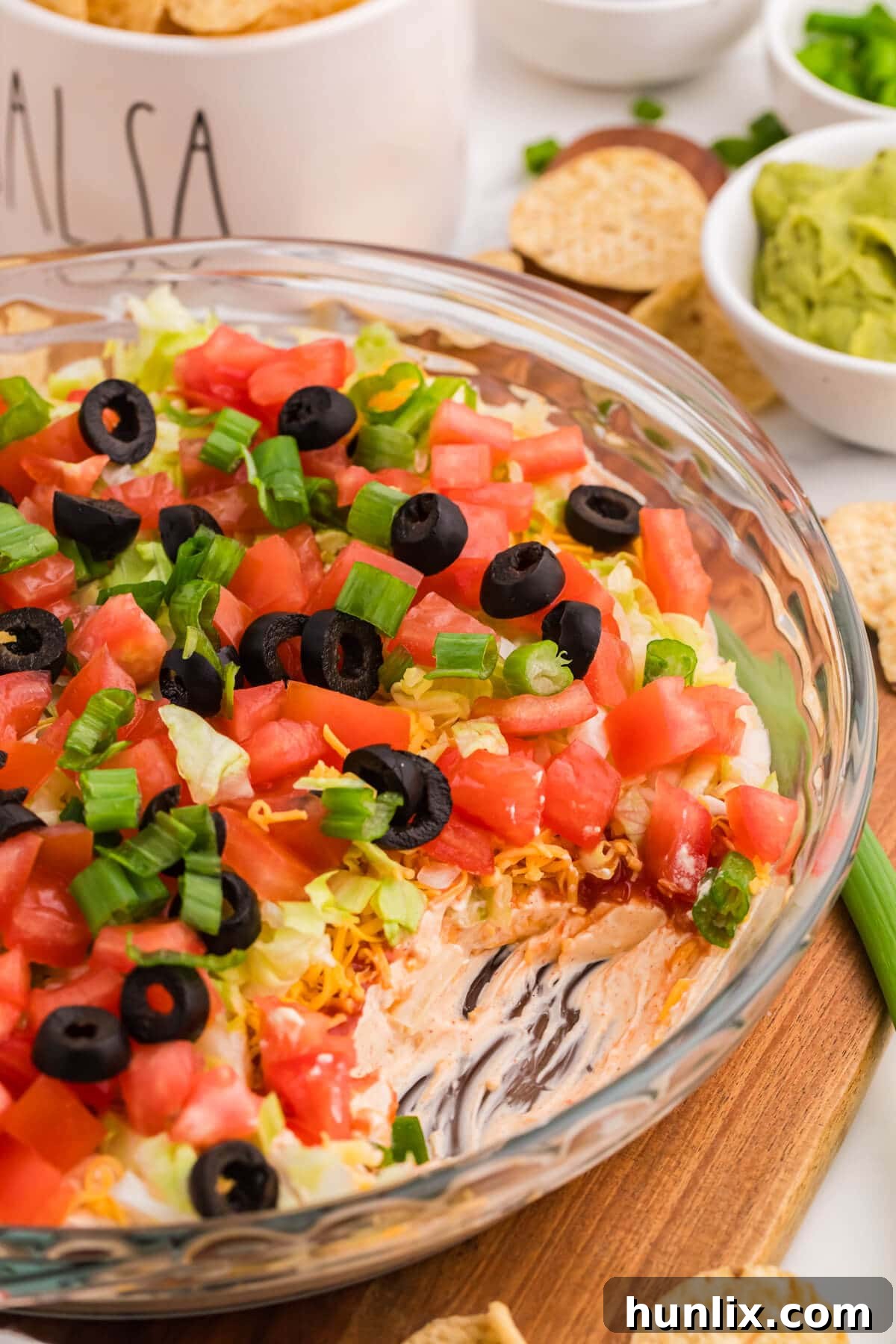 Detailed view of taco dip layers showing creamy base, salsa, cheese, lettuce, and fresh toppings including tomatoes, black olives, and green onions in serving dish.