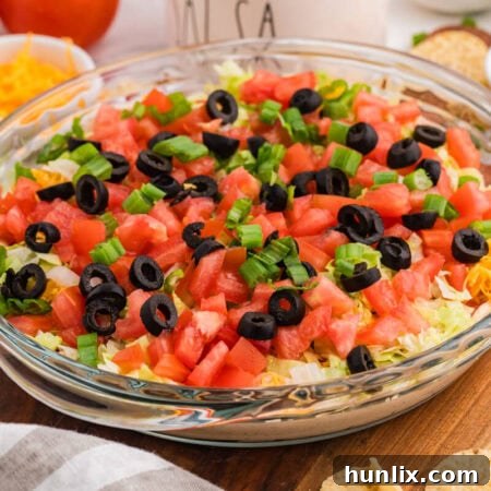 Macro shot of tortilla chip dipped in taco dip with visible layers of sour cream, salsa, shredded cheese, lettuce, and green onions, highlighting creamy texture and fresh toppings.