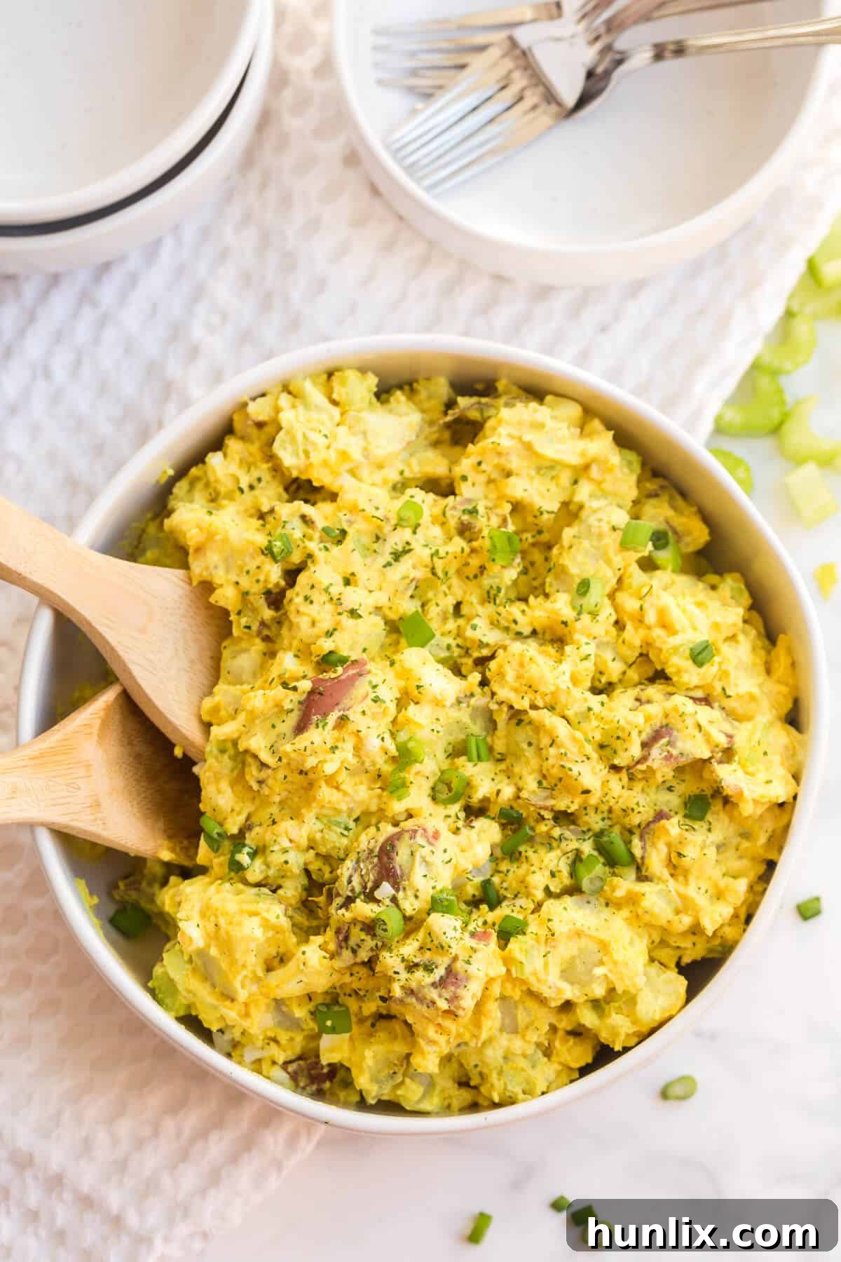 A serving bowl filled with creamy curried potato salad, ready to be served at a summer gathering.