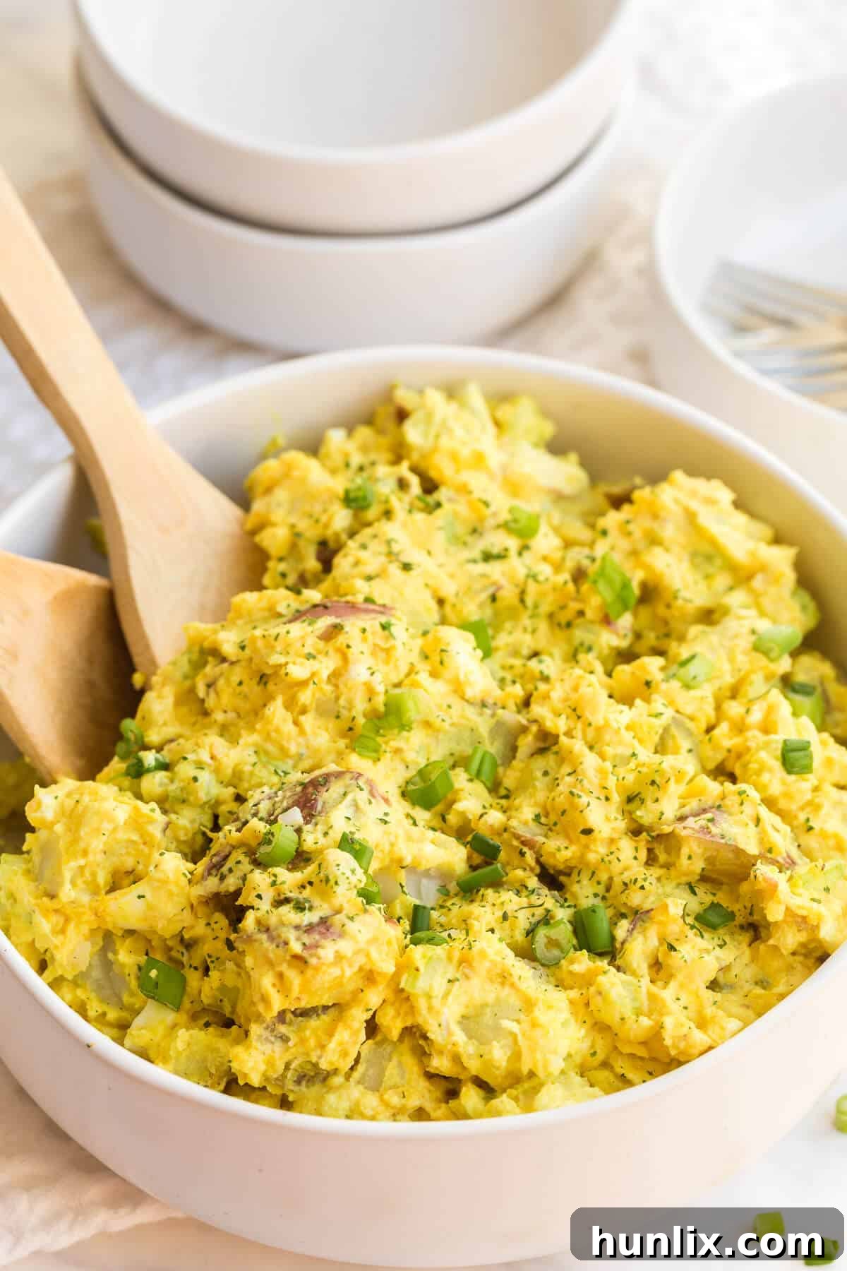 A close-up of curried potato salad with a serving spoon, highlighting the vibrant color and delicious ingredients.